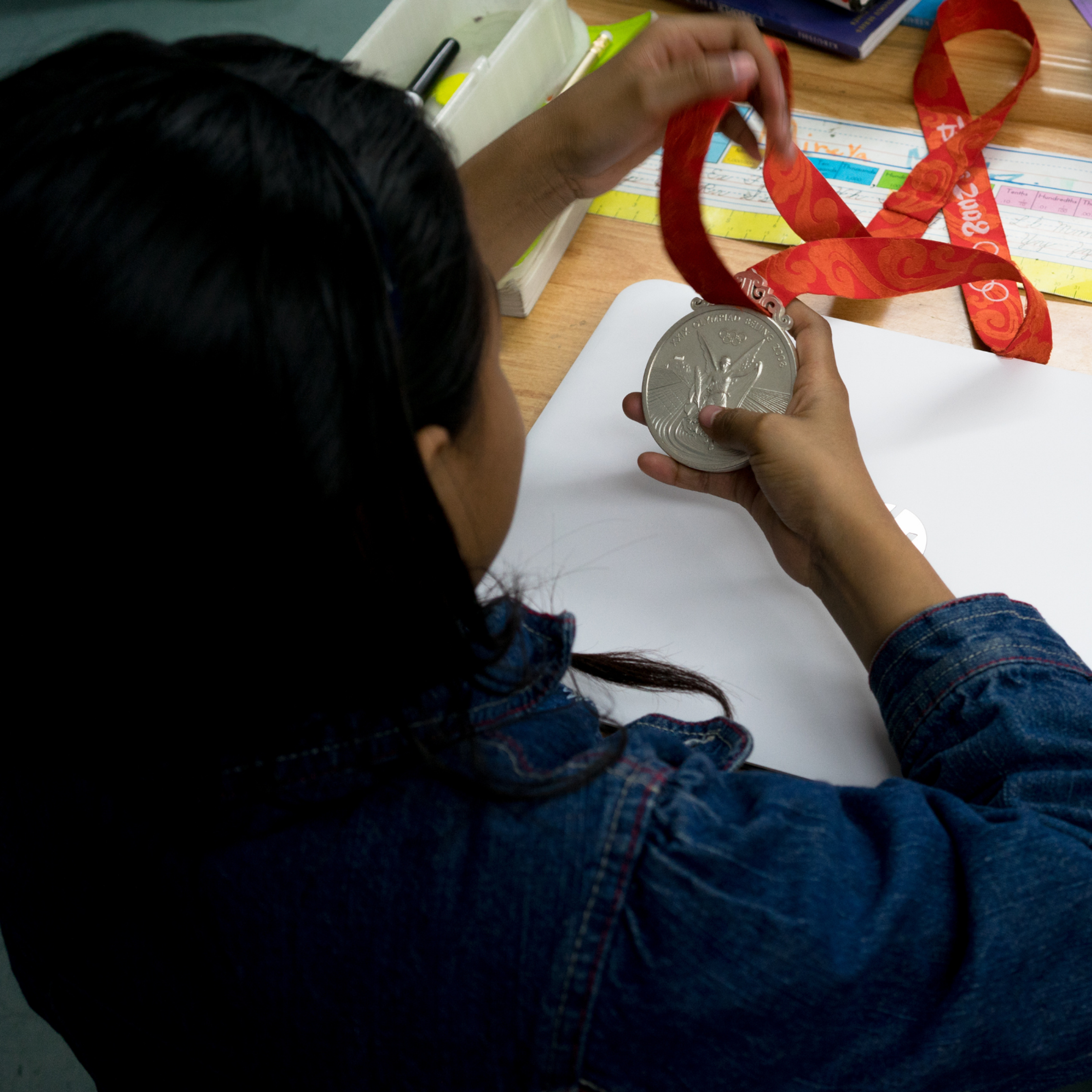 A student examines an athlete mentor's medal at her classroom desk.