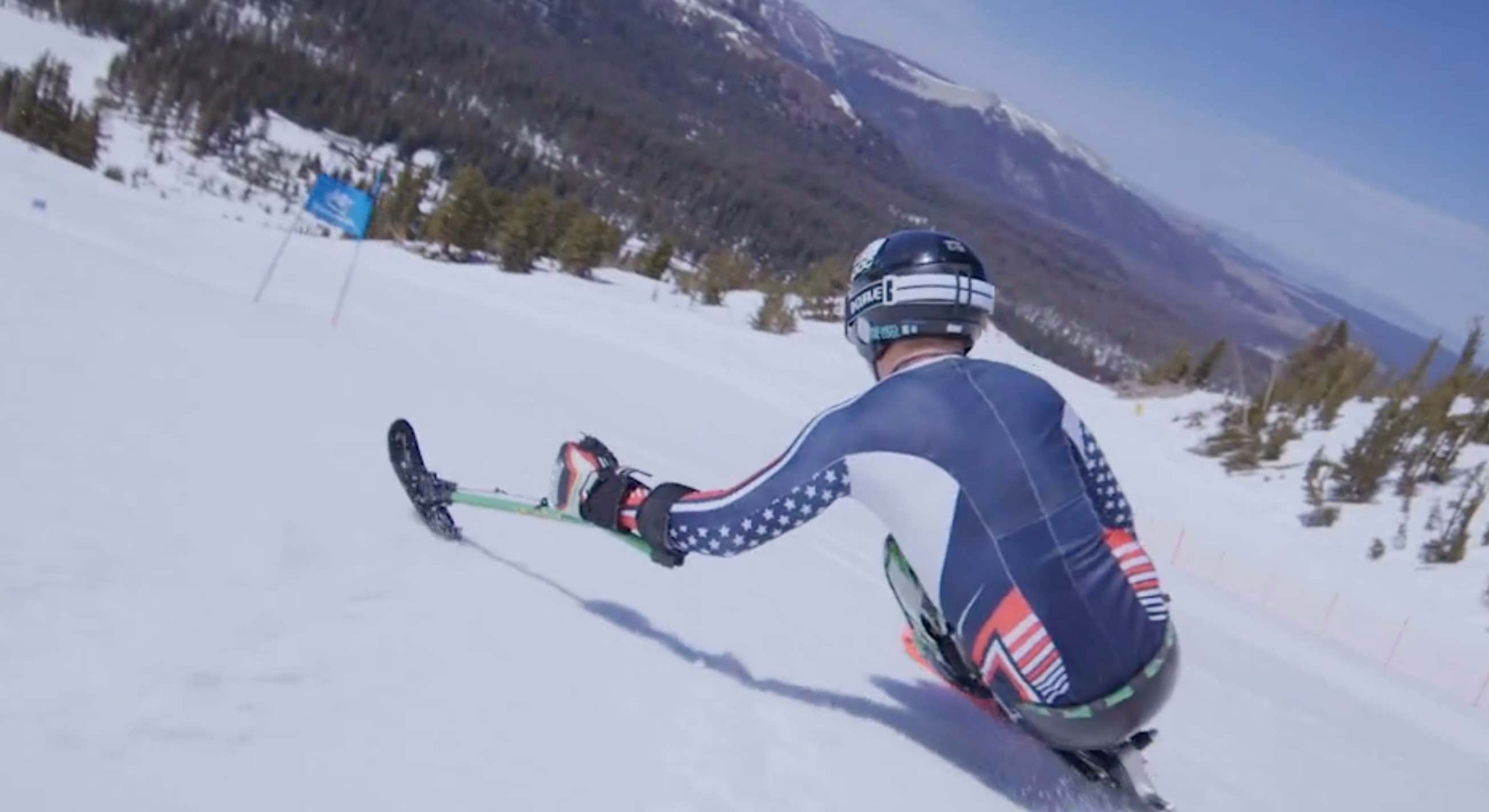 A sit-skier races down a mountain course wearing a Team USA racing suit.
