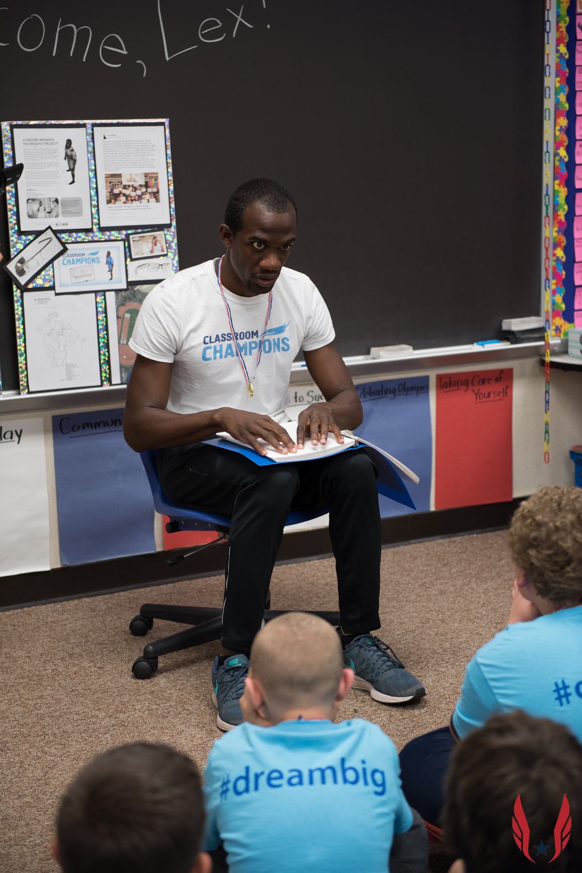 A Classroom Champions mentor speaks with students seated on the floor wearing #dreambig shirts.