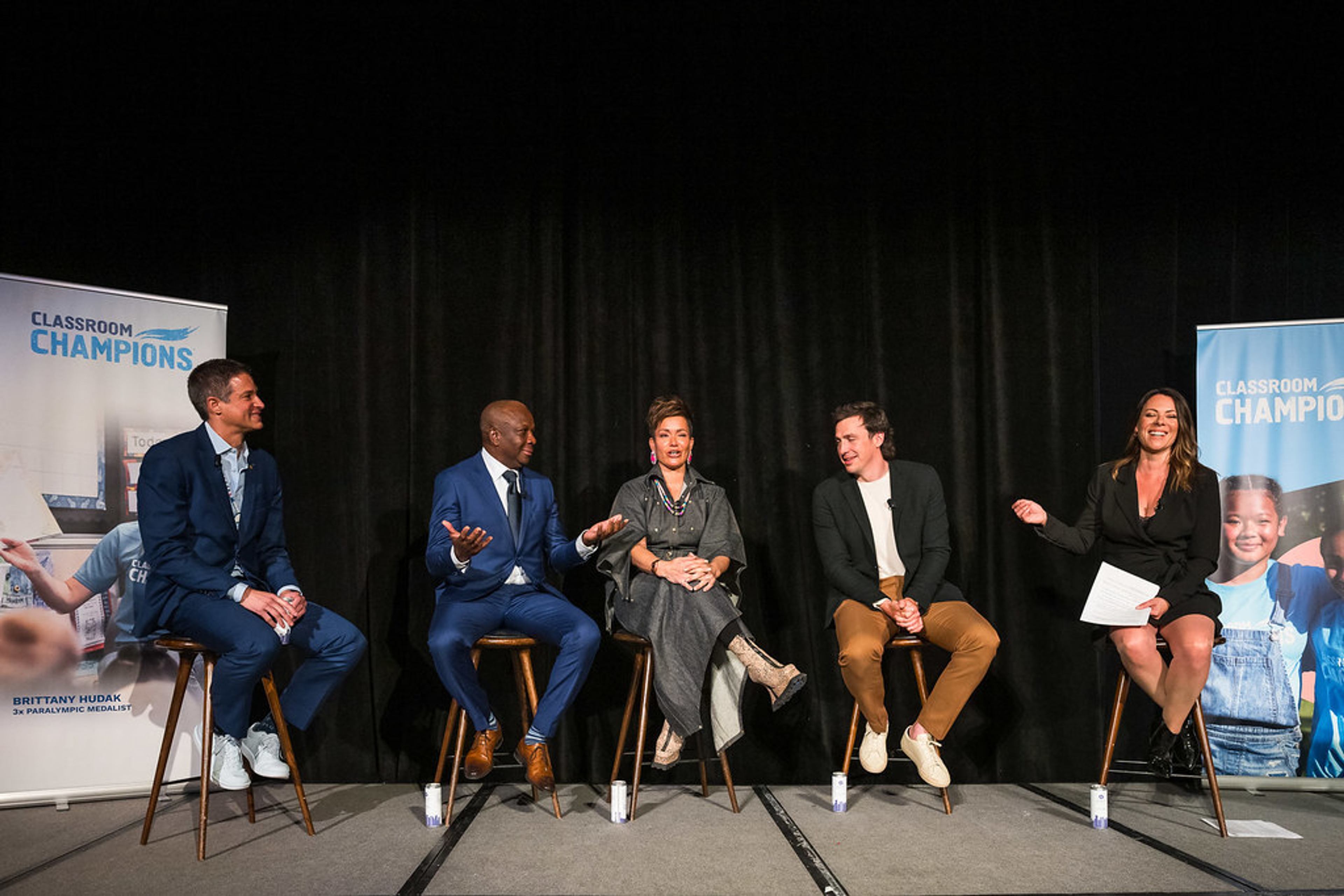 Panelists sit on stools on stage for a discussion at a Classroom Champions event.