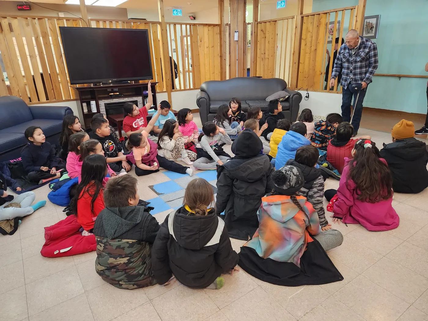 Students sit on the floor listening as a mentor speaks to the classroom.