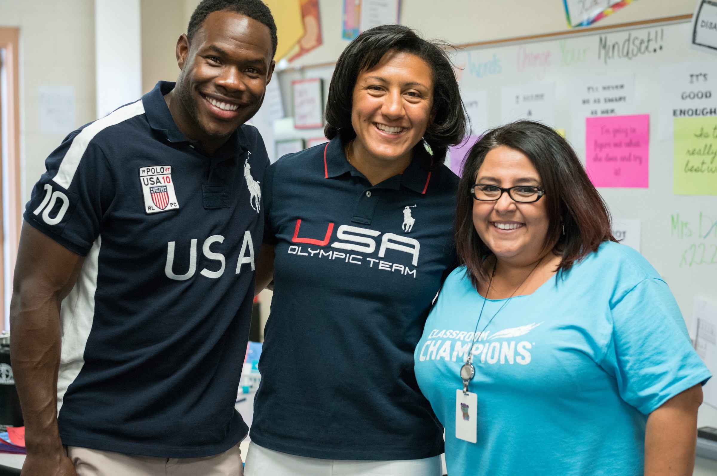 Team USA athletes visit a classroom, posing with a teacher wearing a Classroom Champions shirt.