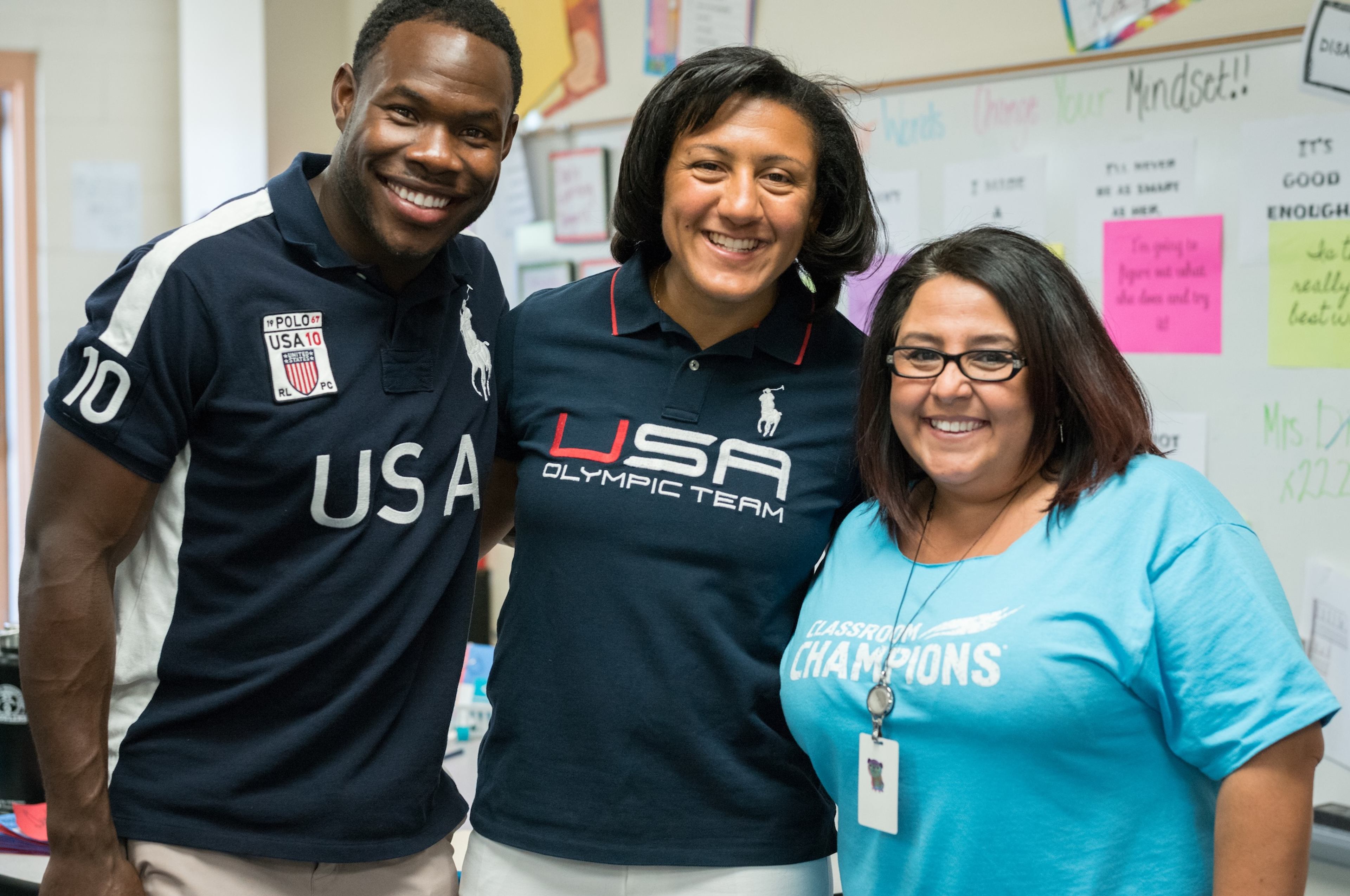 Team USA athletes visit a classroom, posing with a teacher wearing a Classroom Champions shirt.
