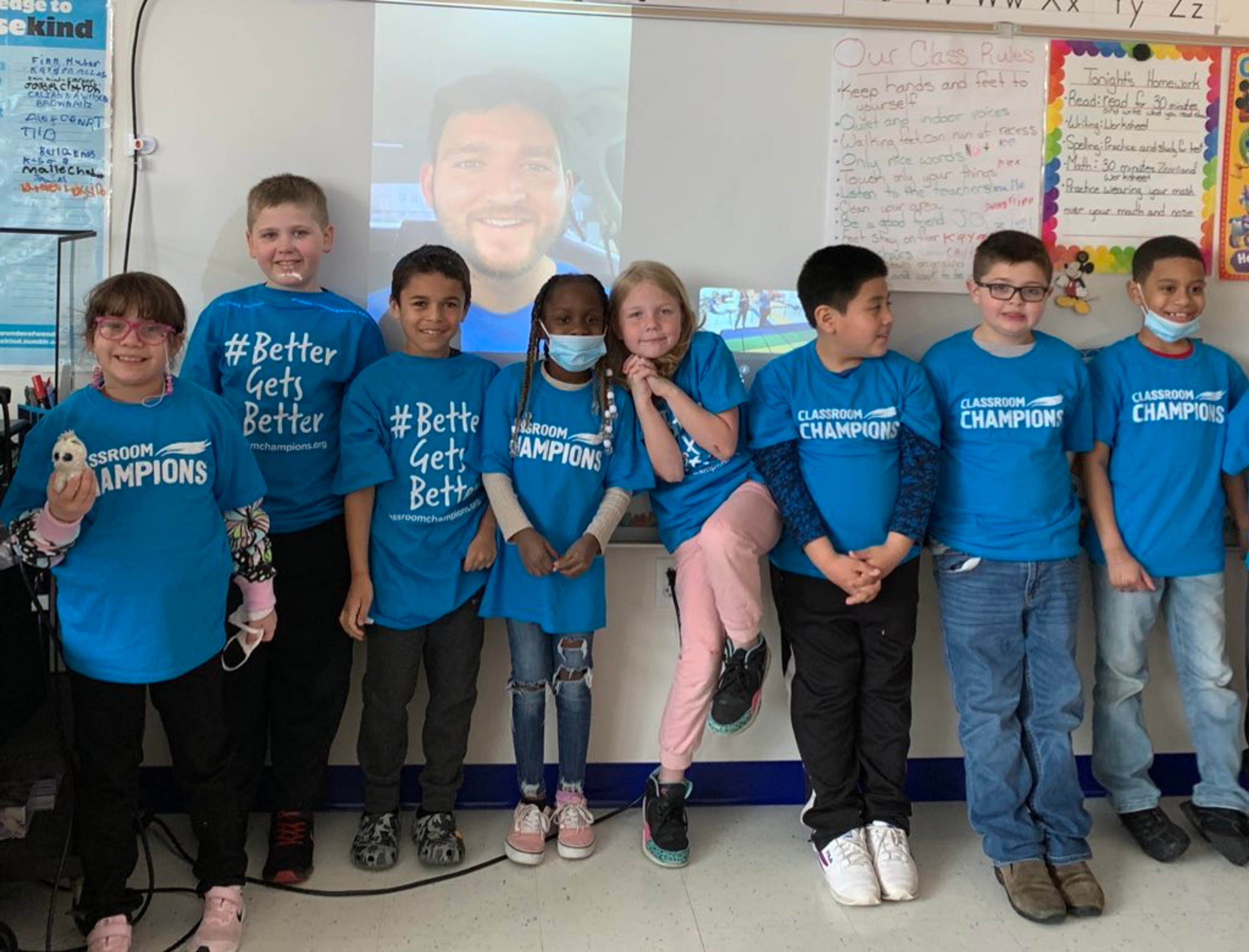 Students in Classroom Champions T-shirts pose together while their athlete mentor smiles on a video call screen behind them.