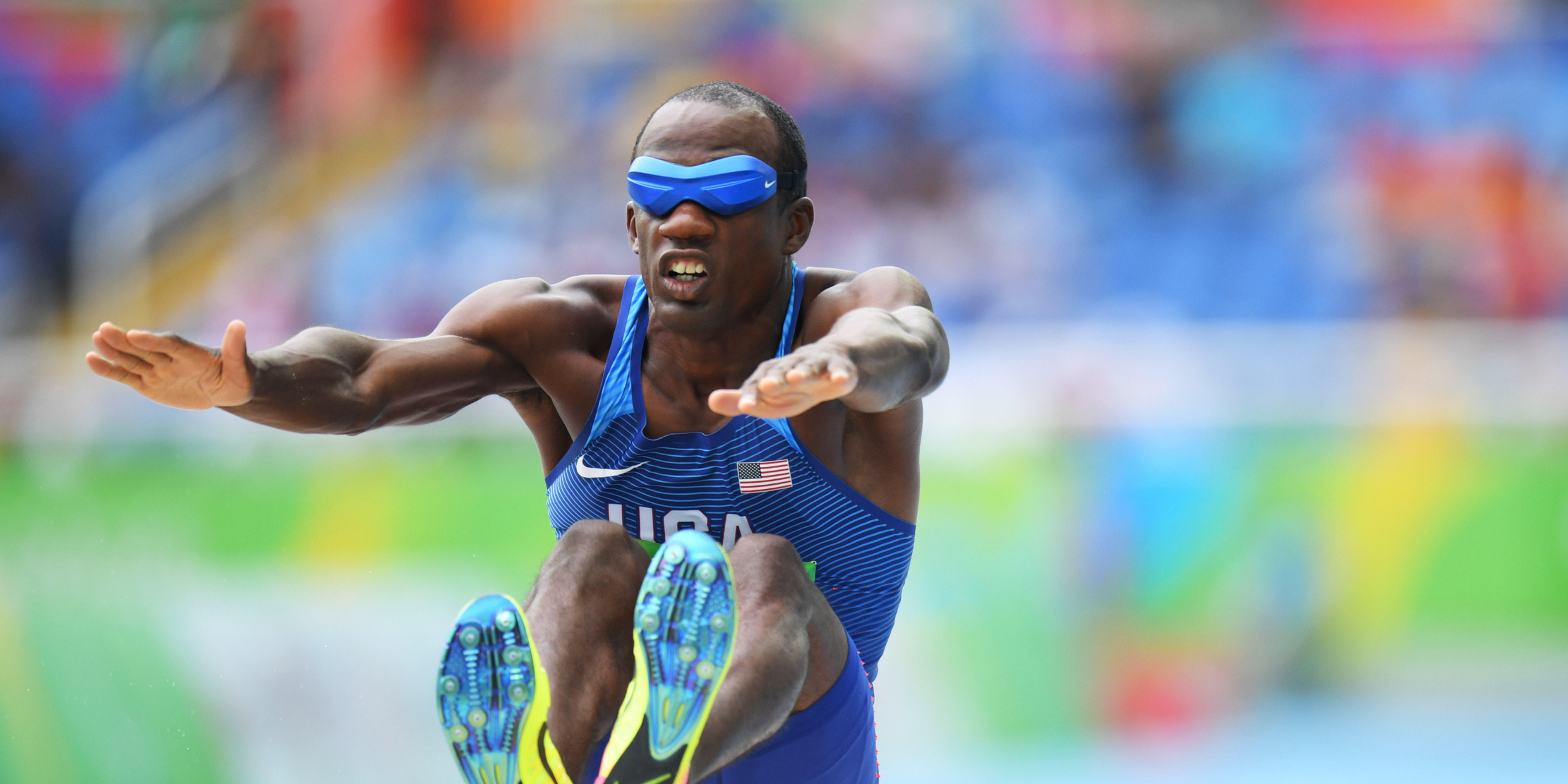 Paralympic long jumper Lex Gillette, wearing a blindfold and Team USA uniform, mid-jump in competition.
