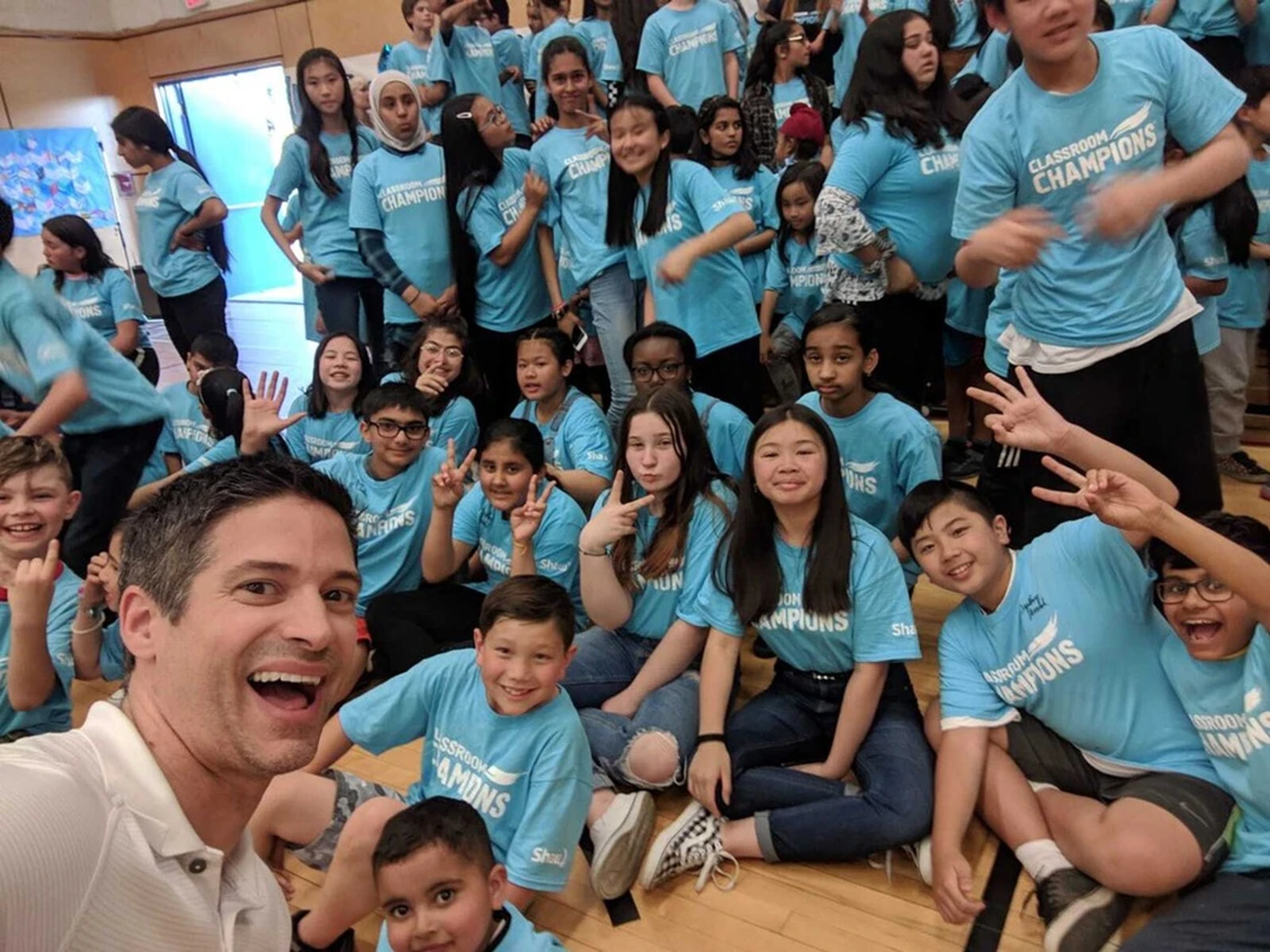 A mentor takes a group selfie with a large class of students wearing Classroom Champions T-shirts.