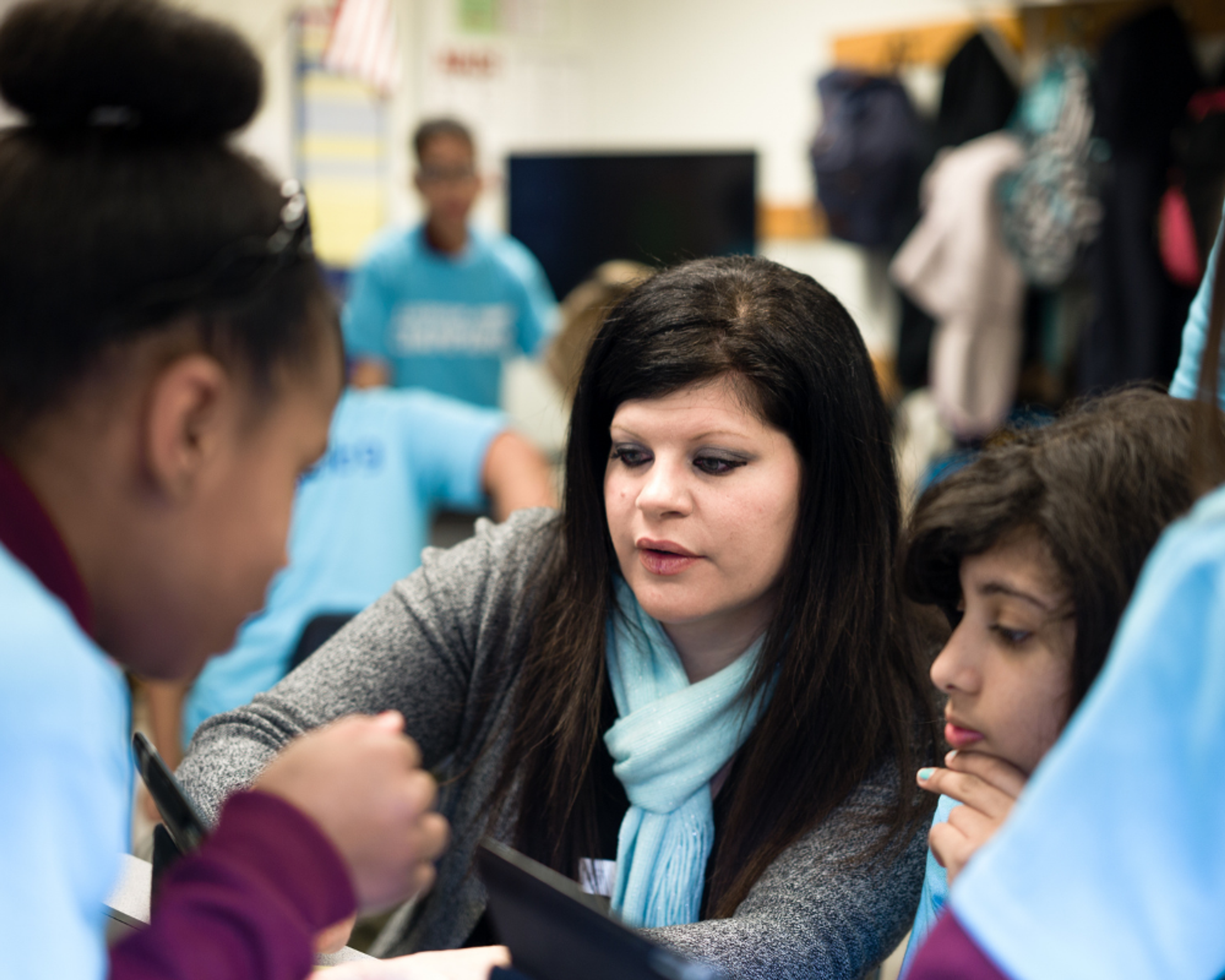 A teacher leans in to talk with students during a classroom activity.