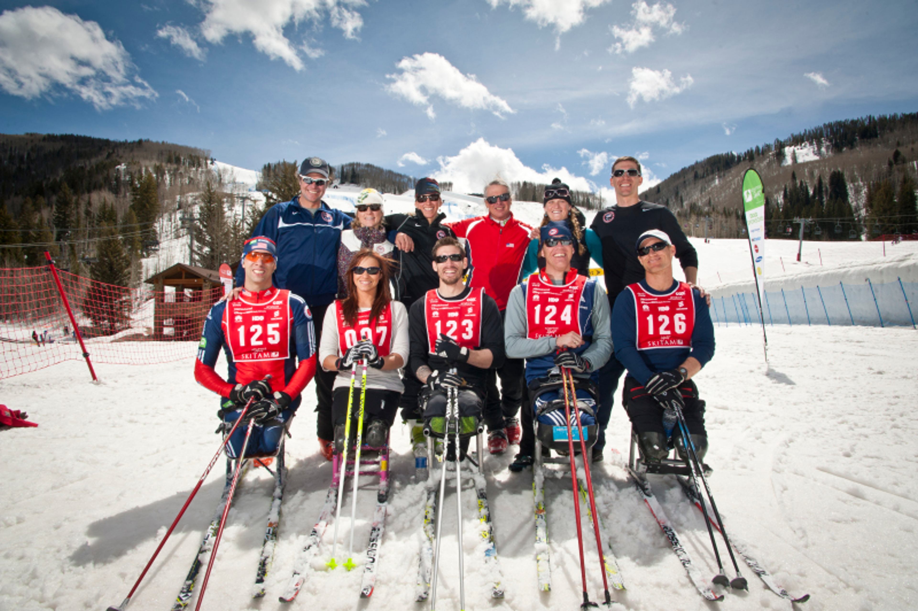 Adaptive ski racers with sit-skis and coaches pose together on a snowy mountain course.