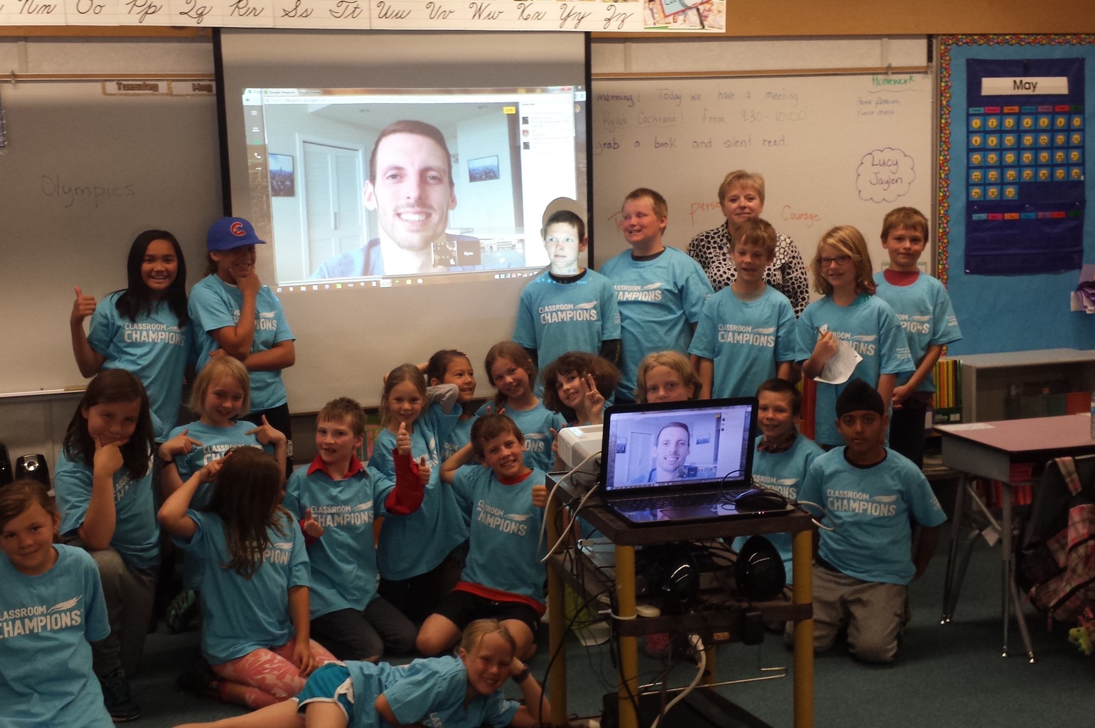 A classroom of students in Classroom Champions shirts video-chat with their athlete mentor projected on screen.