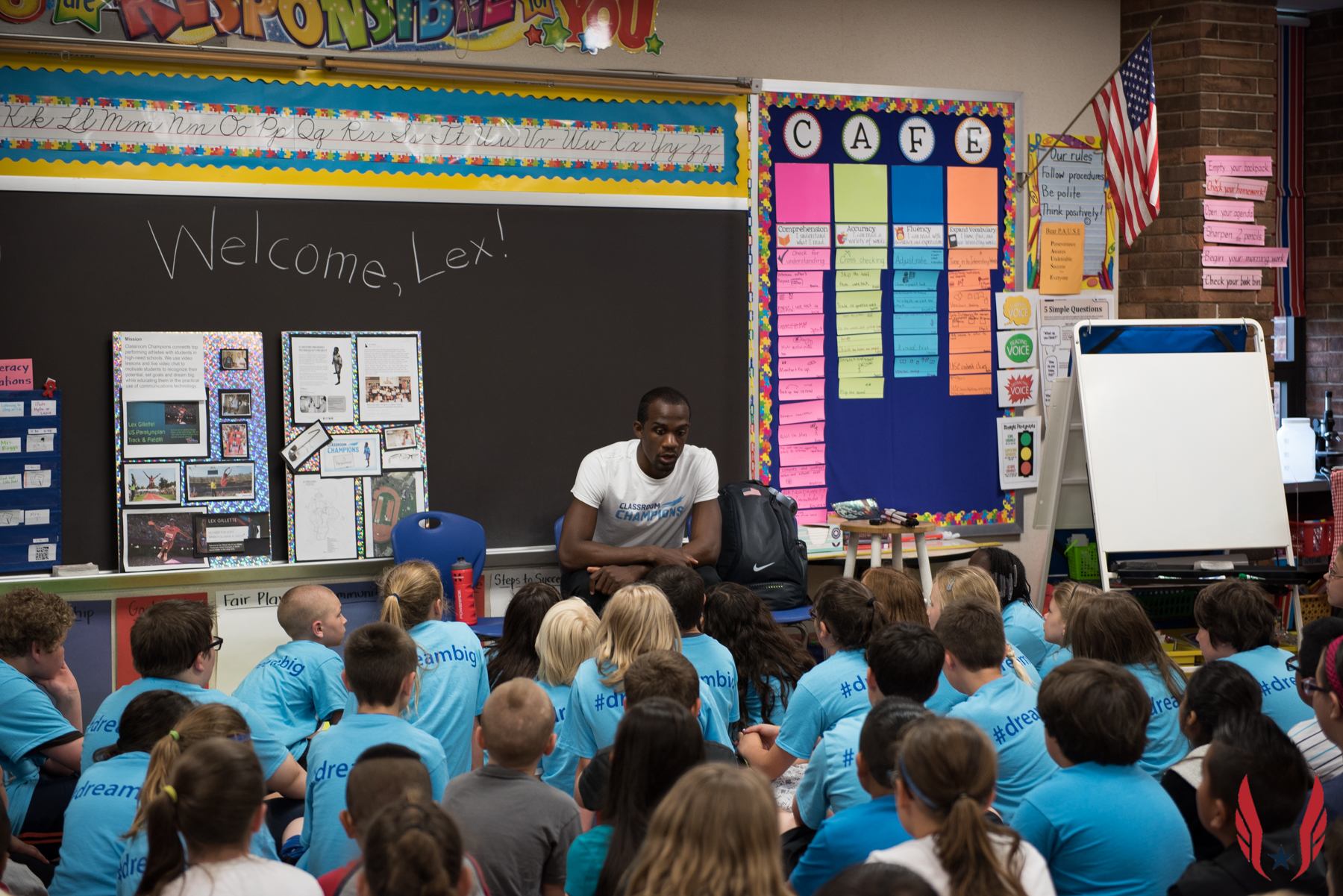 Athlete mentor Lex speaks to students wearing #dreambig shirts seated in a classroom decorated with student work.