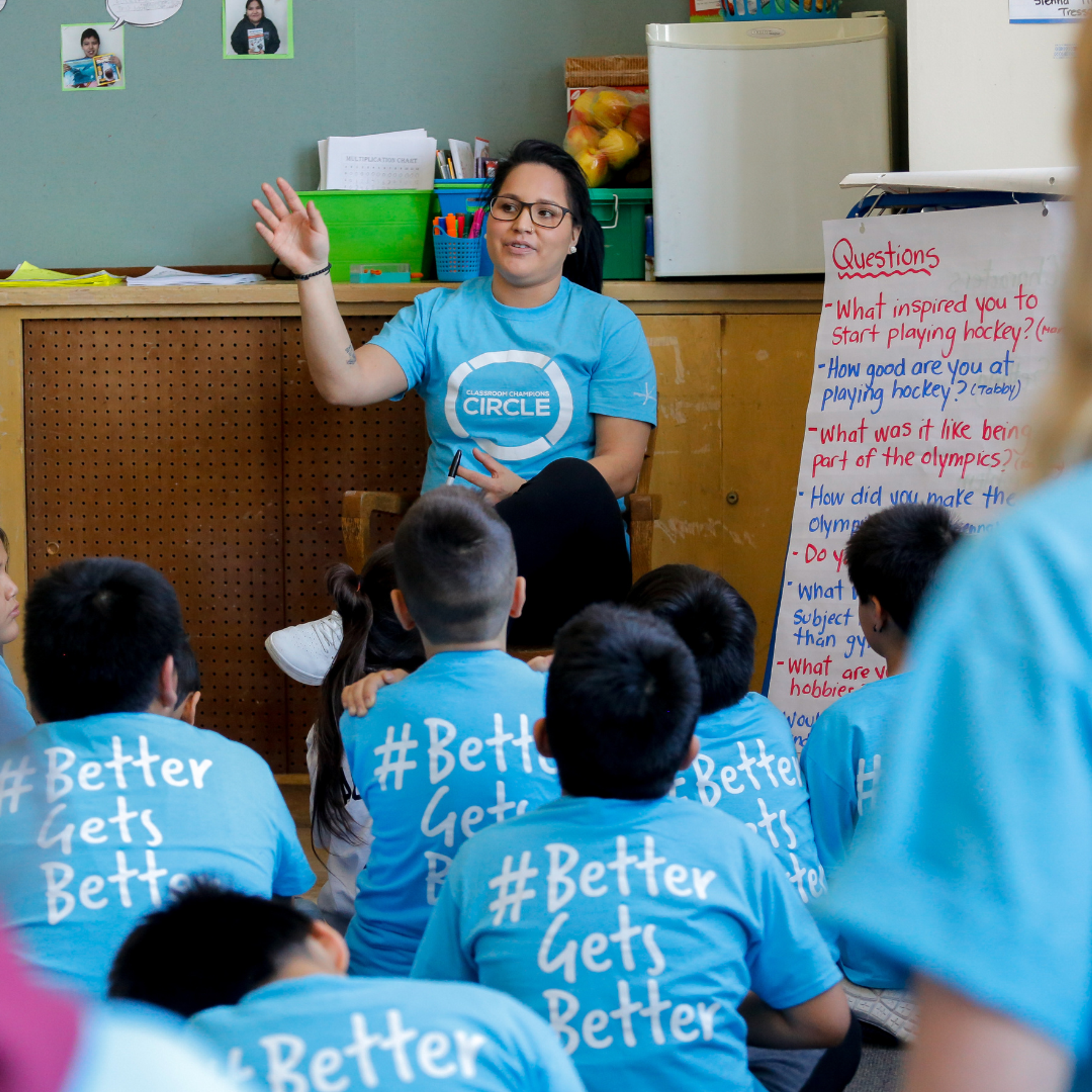 A Classroom Champions Circle mentor answers student questions in a classroom wearing #BetterGetsBetter shirts.