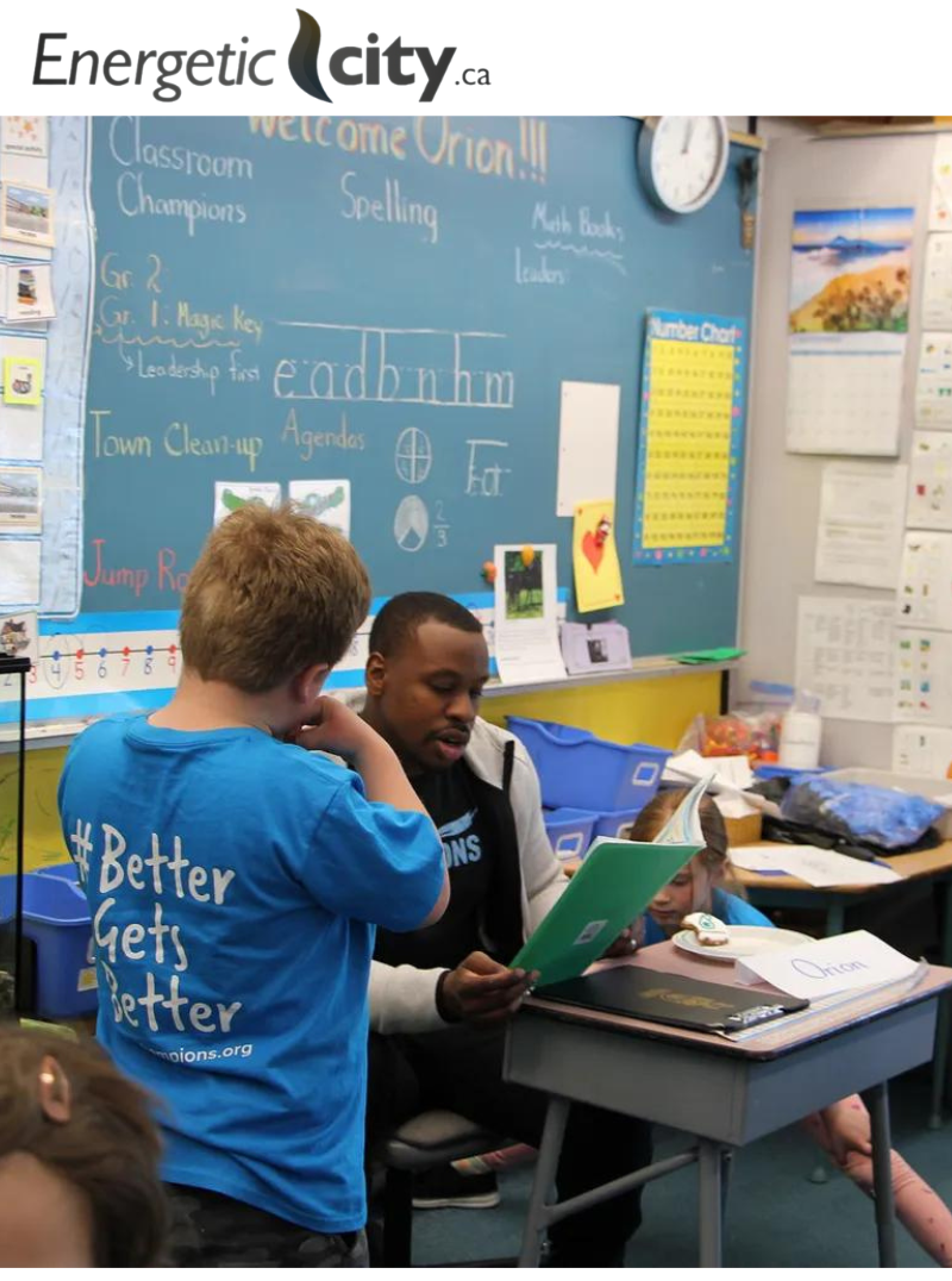 A Classroom Champions mentor reads with students in a classroom decorated with a chalkboard welcoming him.