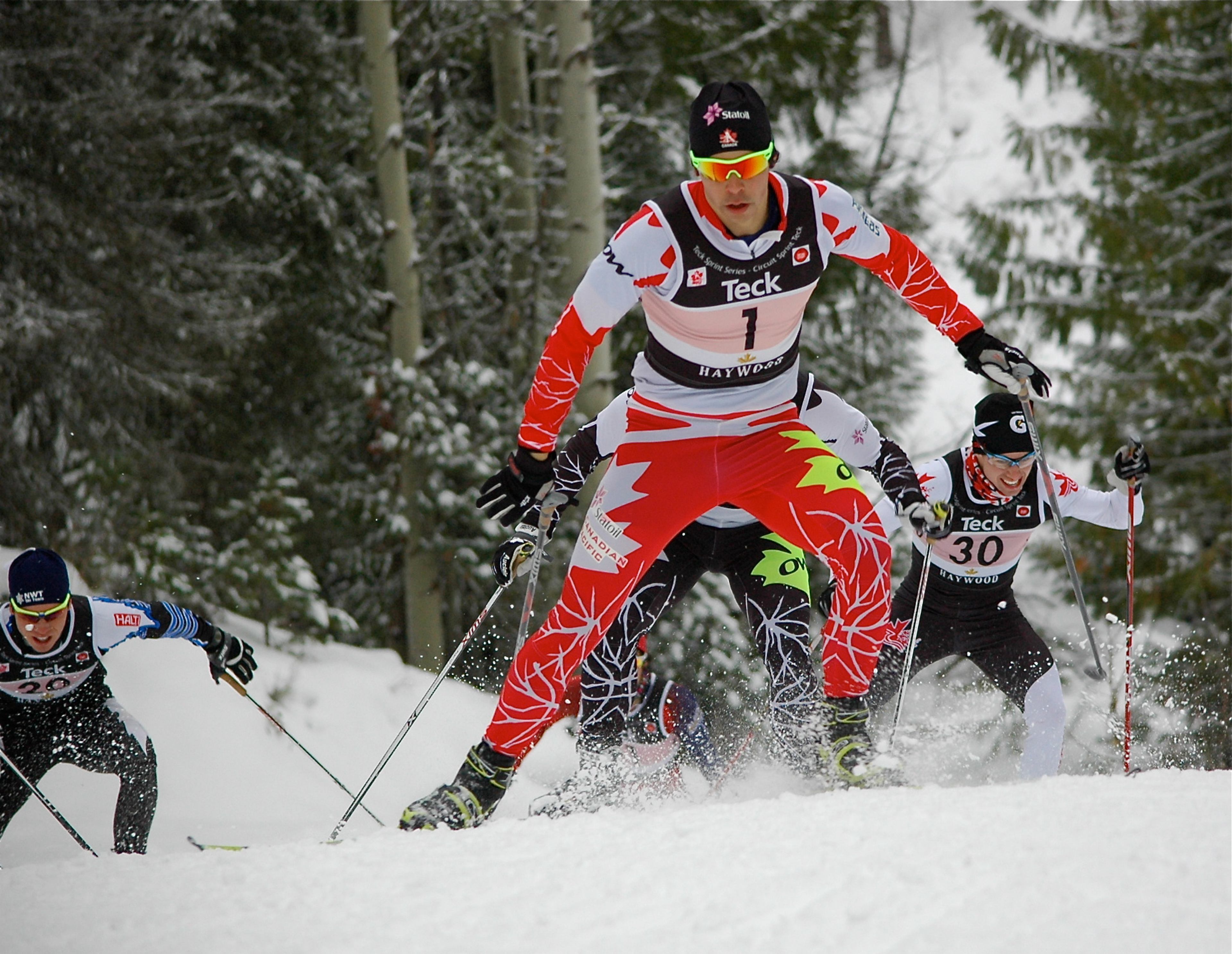 Cross-country skiers race through a snowy forest course during a competition.