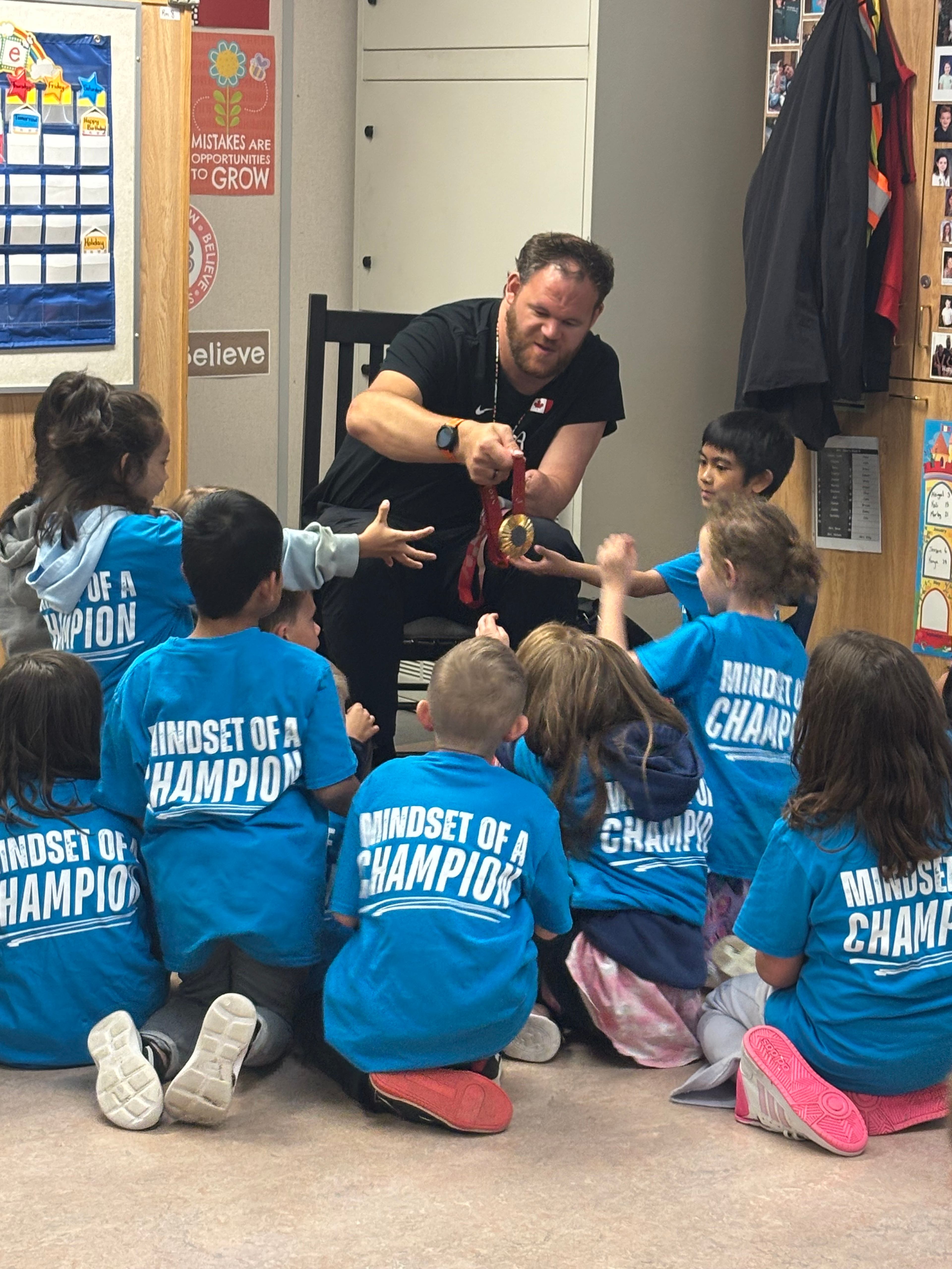 An athlete mentor shows his medal to students wearing "Mindset of a Champion" shirts during a classroom visit.