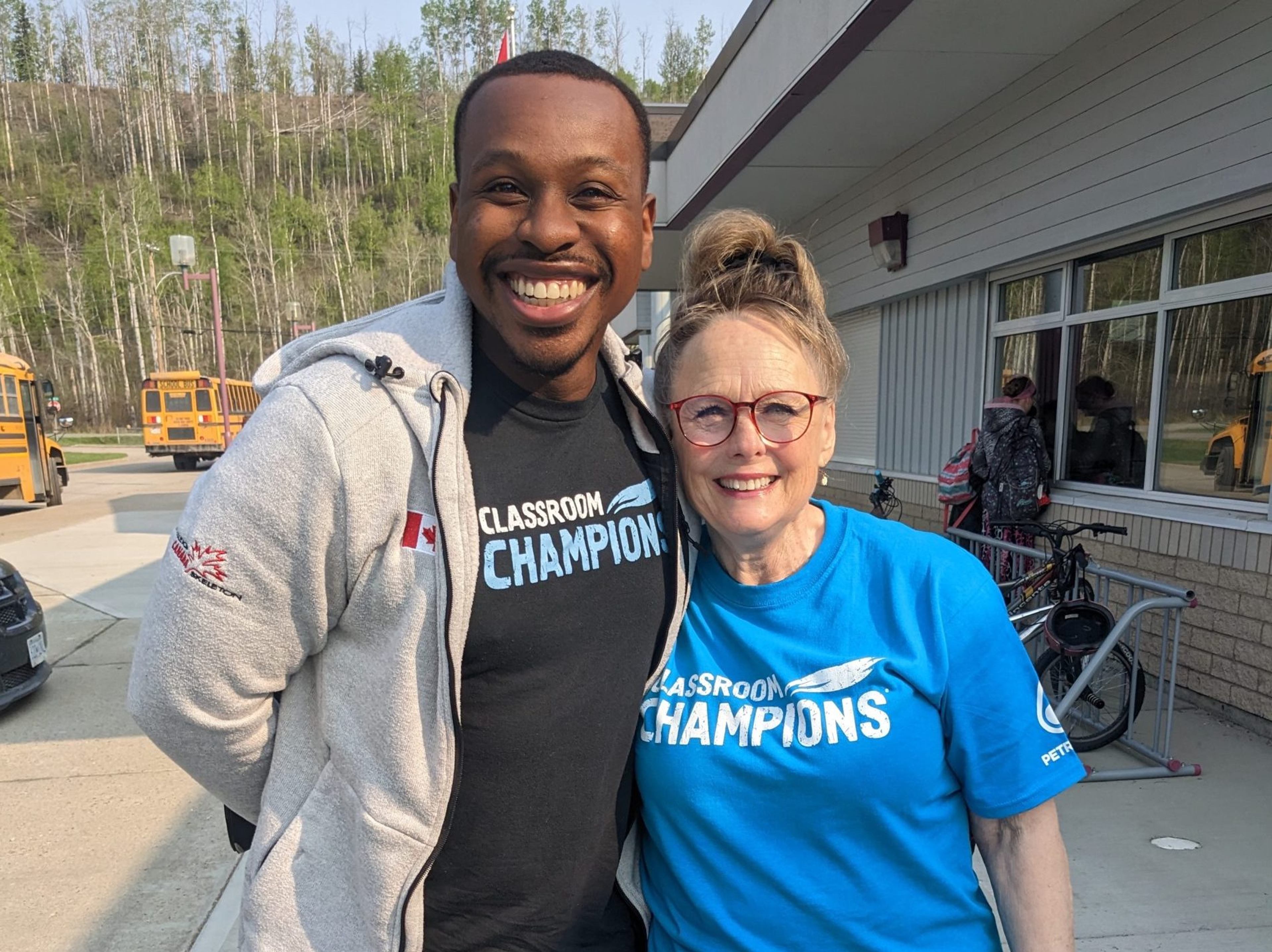 An athlete mentor and educator wearing Classroom Champions shirts smile together outside a school.
