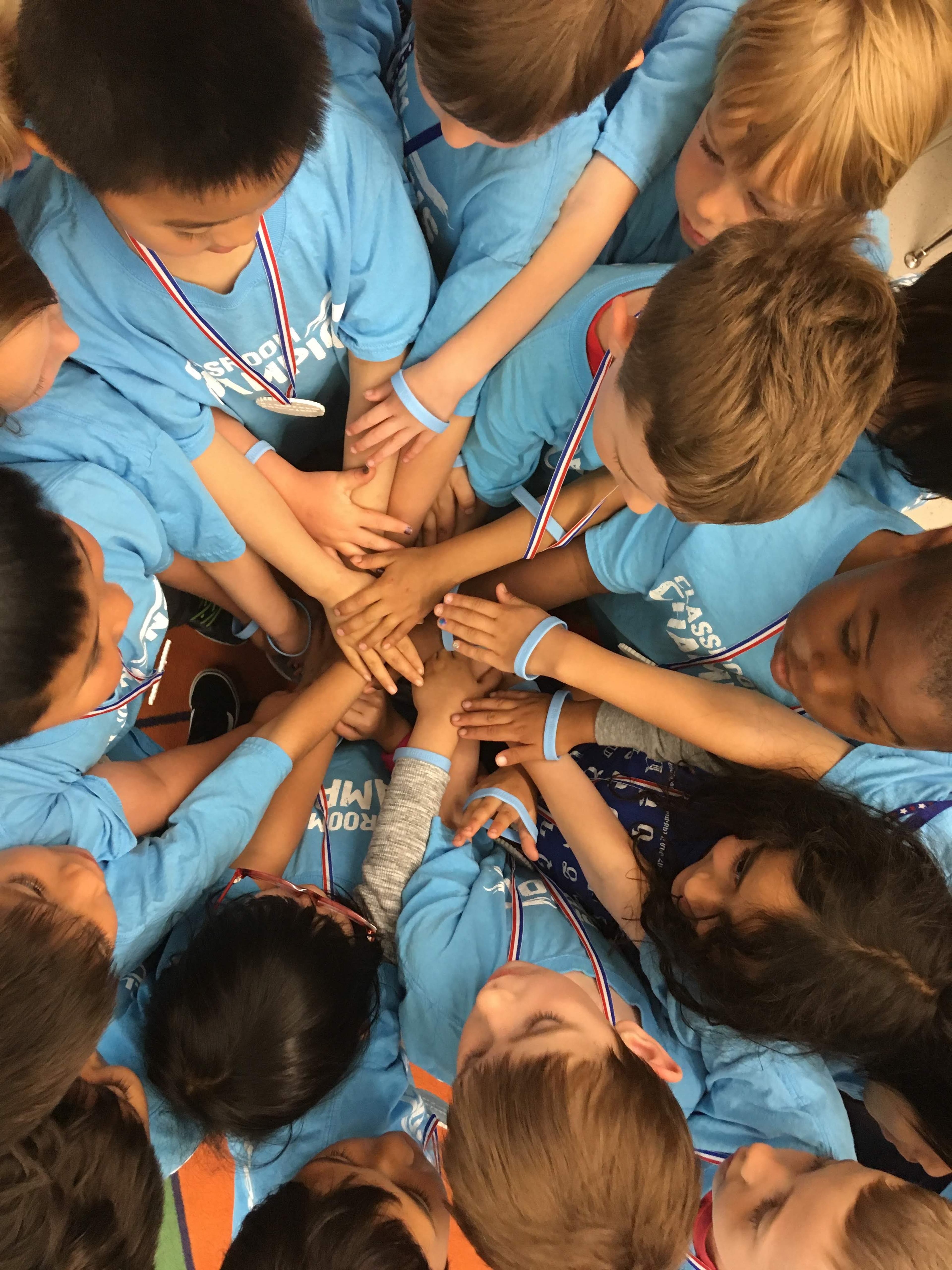 Students in Classroom Champions shirts and medals stack their hands together in a team huddle.