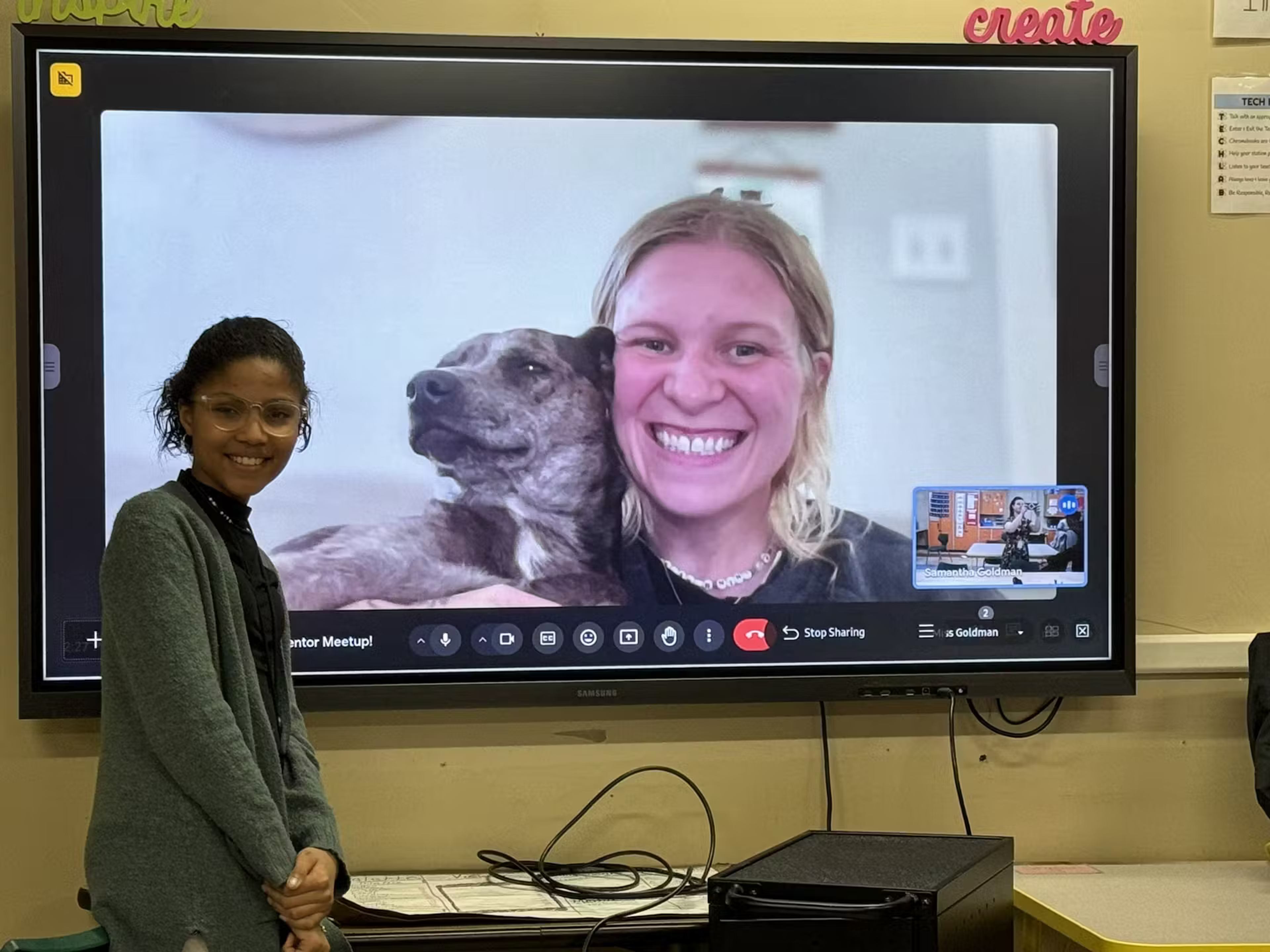 A student stands smiling beside a screen showing a mentor video call during a Champions Circle meetup.