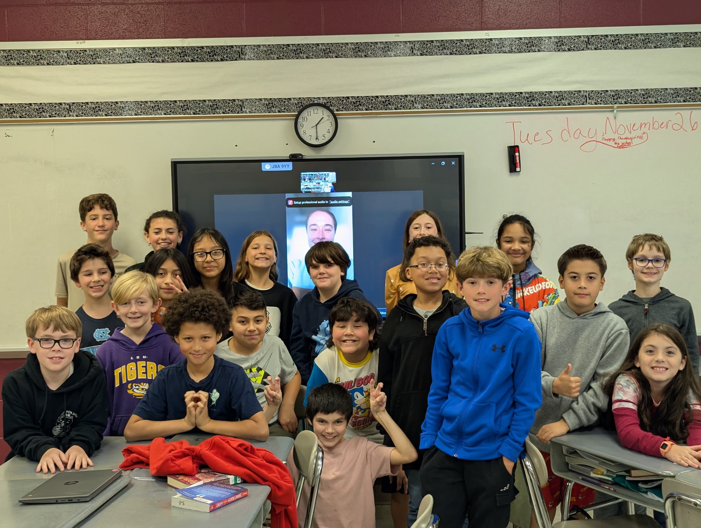 A classroom of students gather for a photo during a live video call with their athlete mentor.