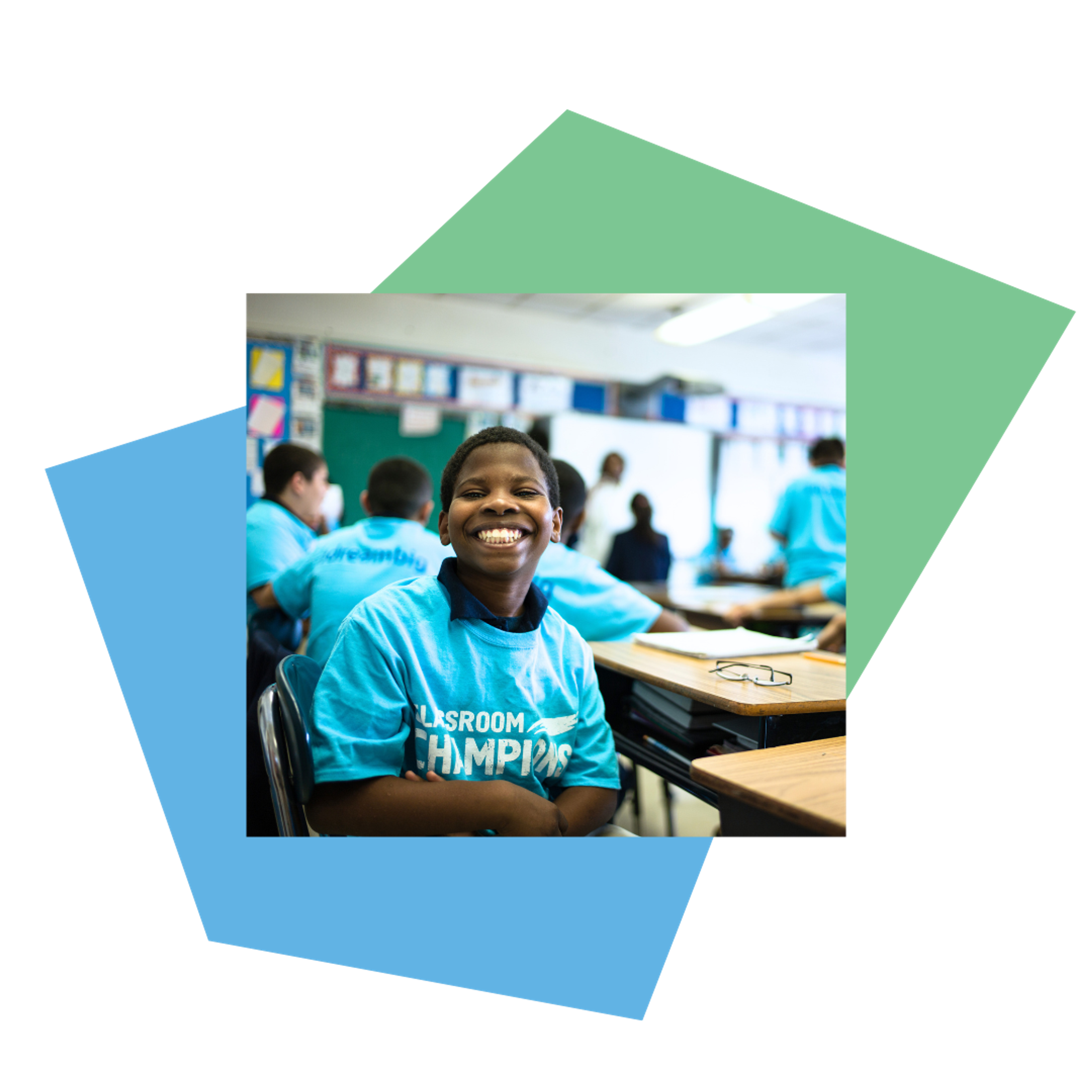 A smiling student in a Classroom Champions t-shirt sits at his desk with classmates.