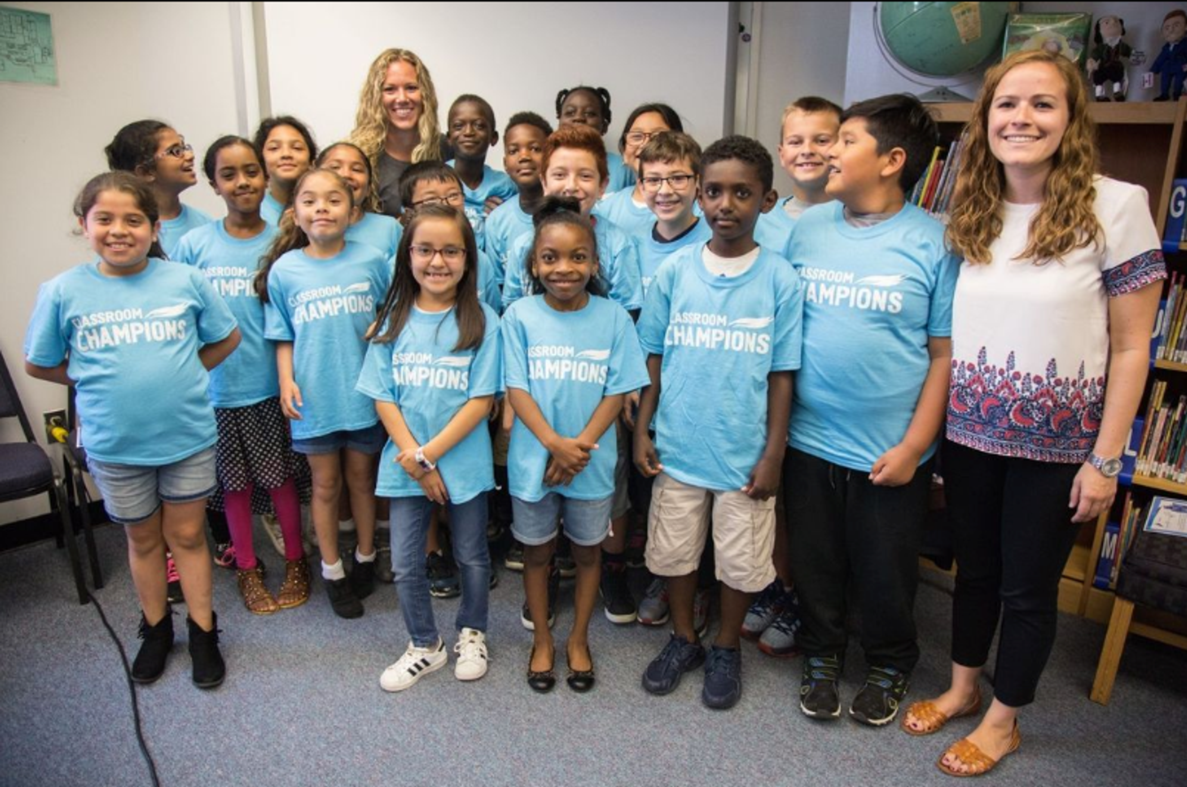 A classroom of students and their teachers pose together wearing Classroom Champions T-shirts.
