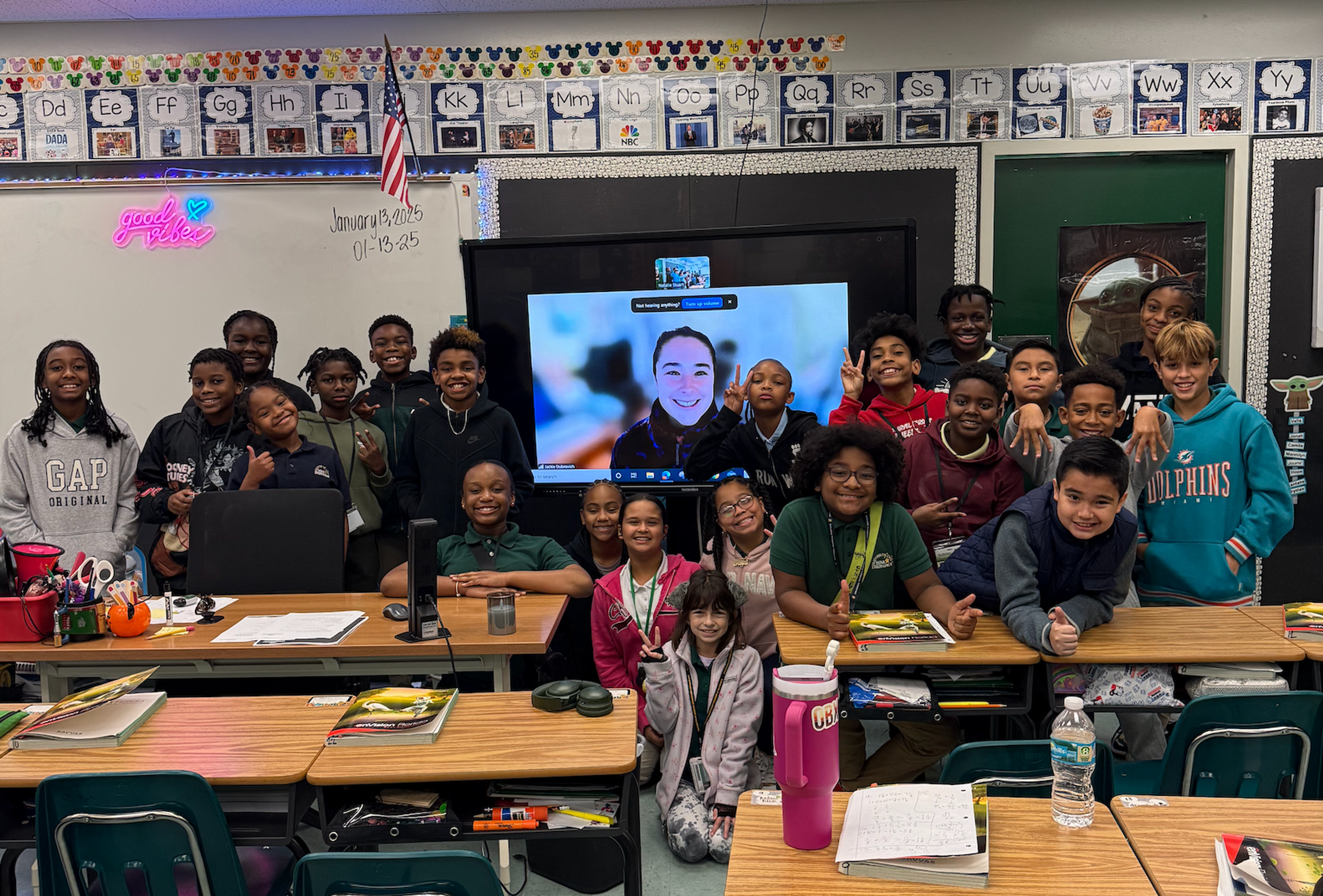 A fifth-grade class gathers around a screen for a live video chat with their Classroom Champions mentor.
