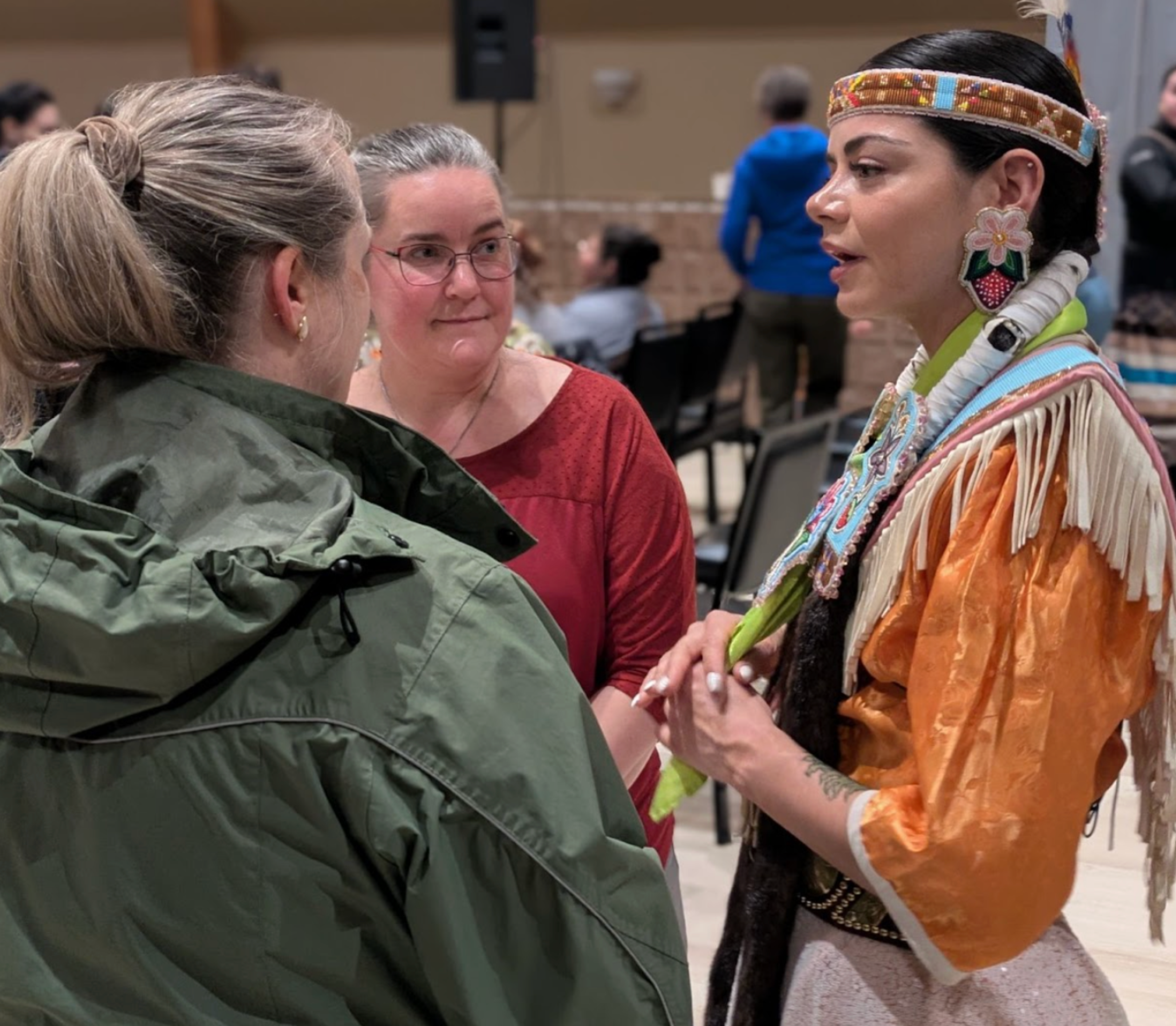 A woman in traditional beaded regalia speaks with visitors during the Chisasibi community visit.