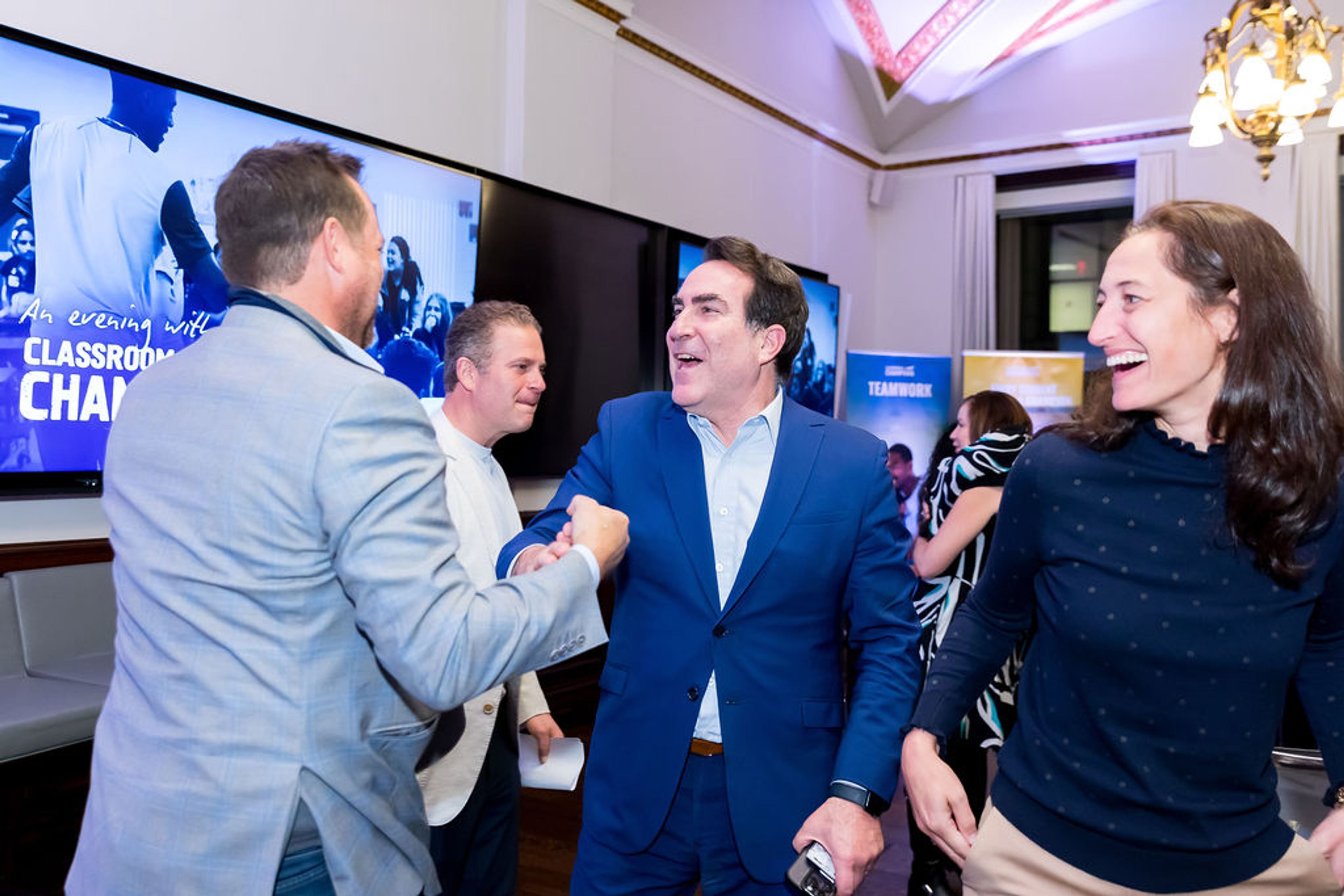 Guests shake hands and laugh at an evening event for Classroom Champions supporters.