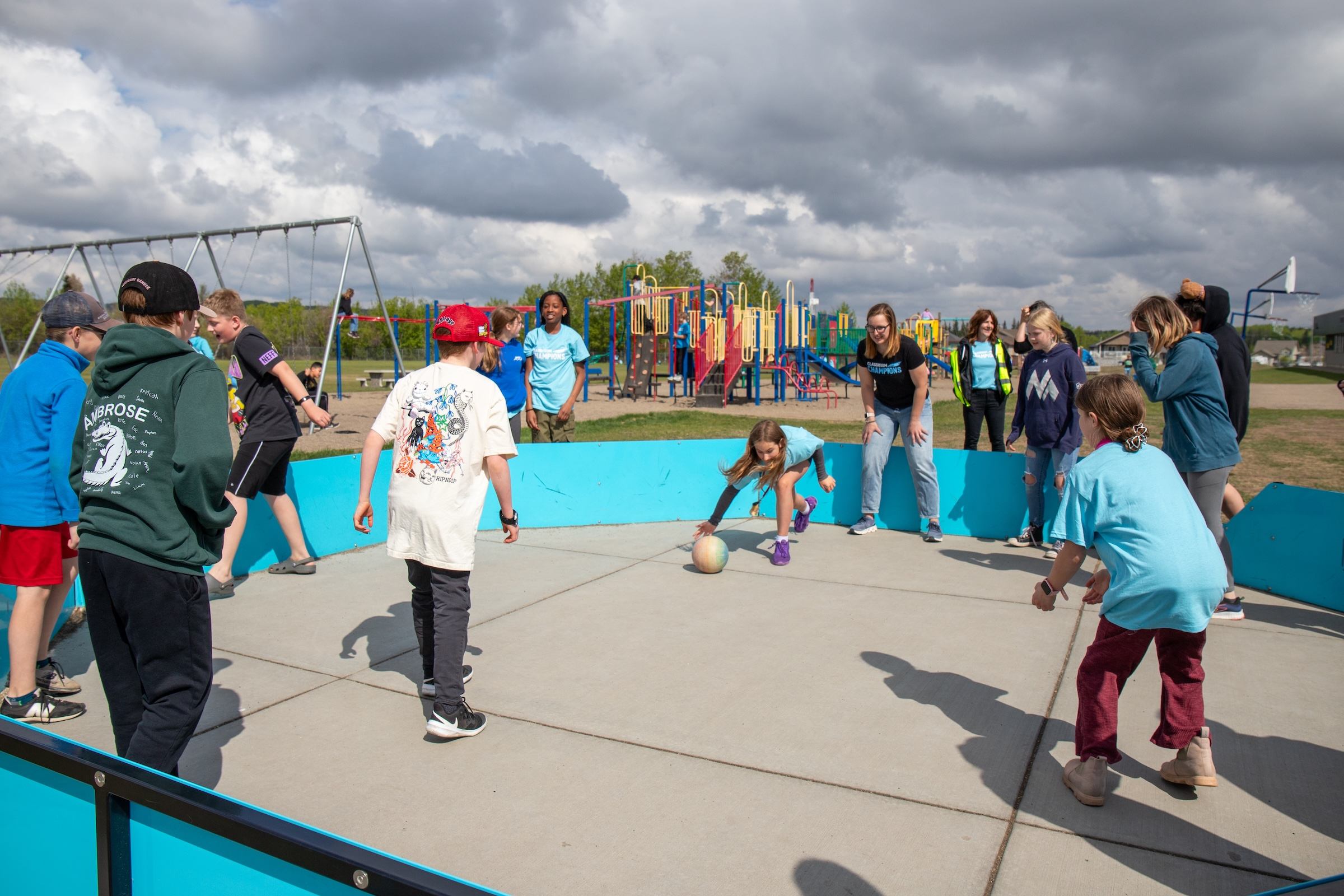 Students play a game together on an outdoor court near a playground during a mentor visit.