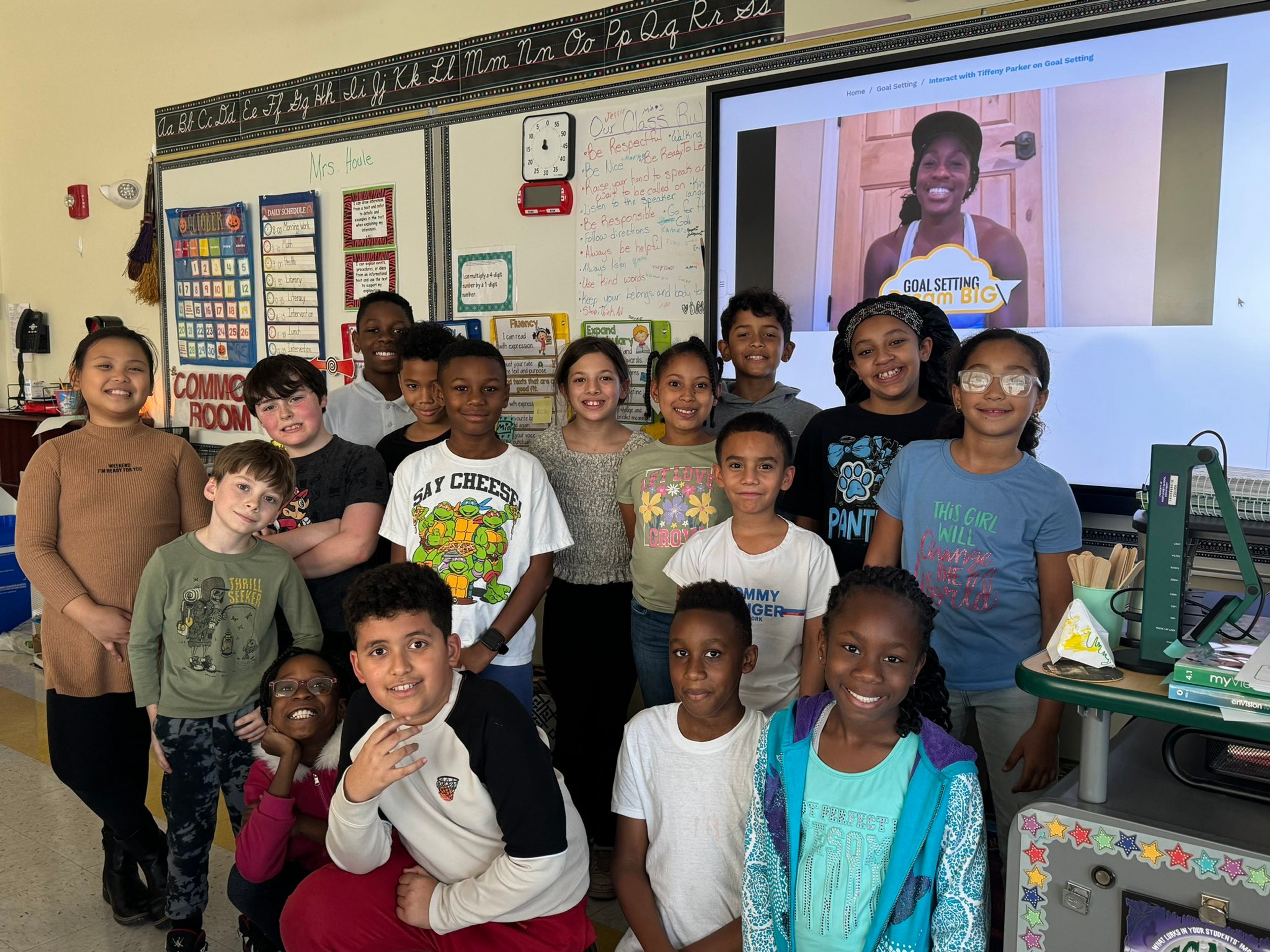 A classroom of students poses together as athlete mentor Tiffany Parker appears on screen for a goal-setting lesson.