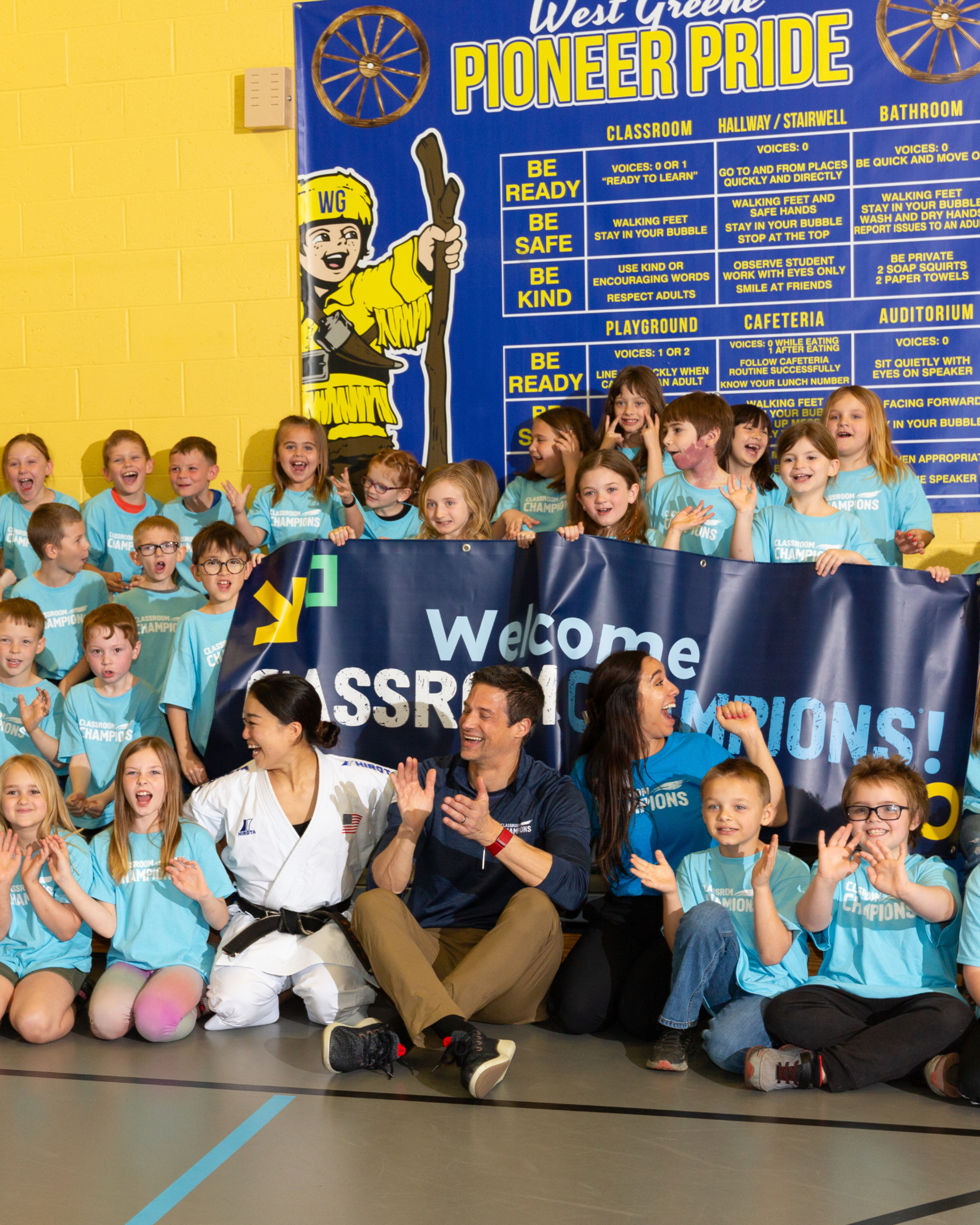 Excited students and mentors cheer behind a banner welcoming Classroom Champions at West Greene school.