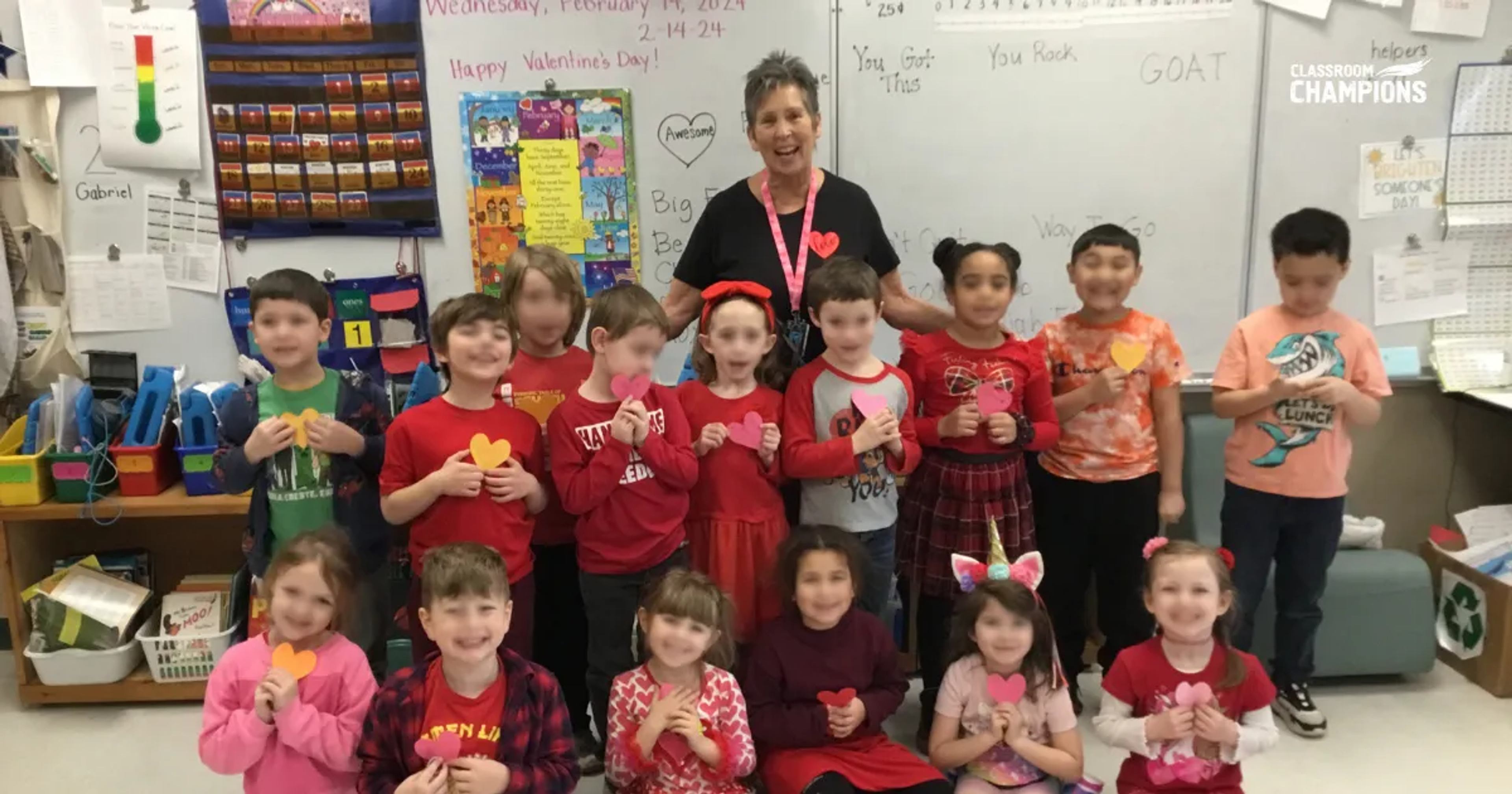 A class celebrates Valentine's Day with their teacher, each holding a paper heart.