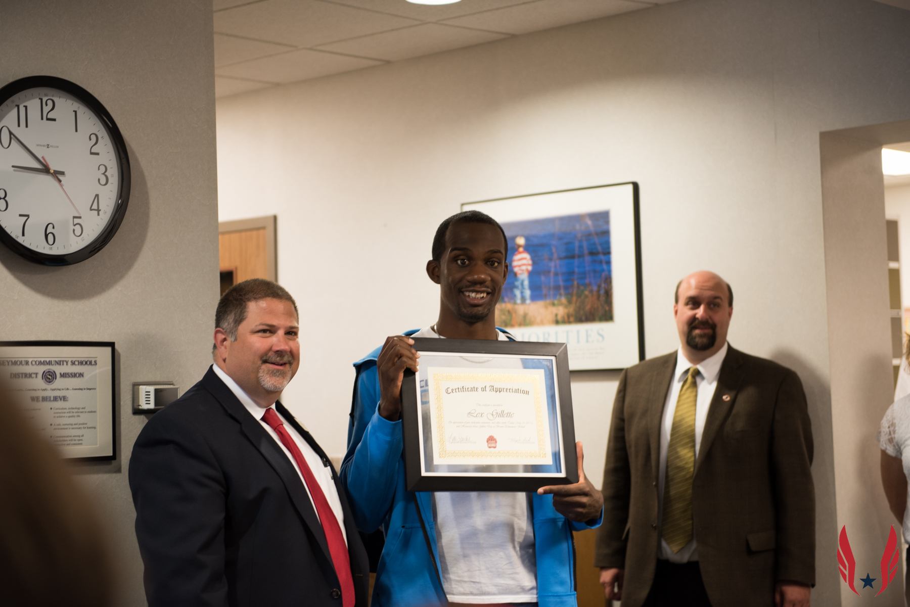 A student holds a framed Certificate of Appreciation while standing with two school administrators.