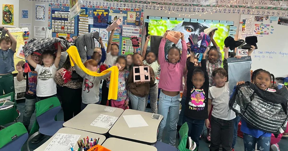 Elementary students hold up winter coats and scarves collected for a classroom clothing drive.