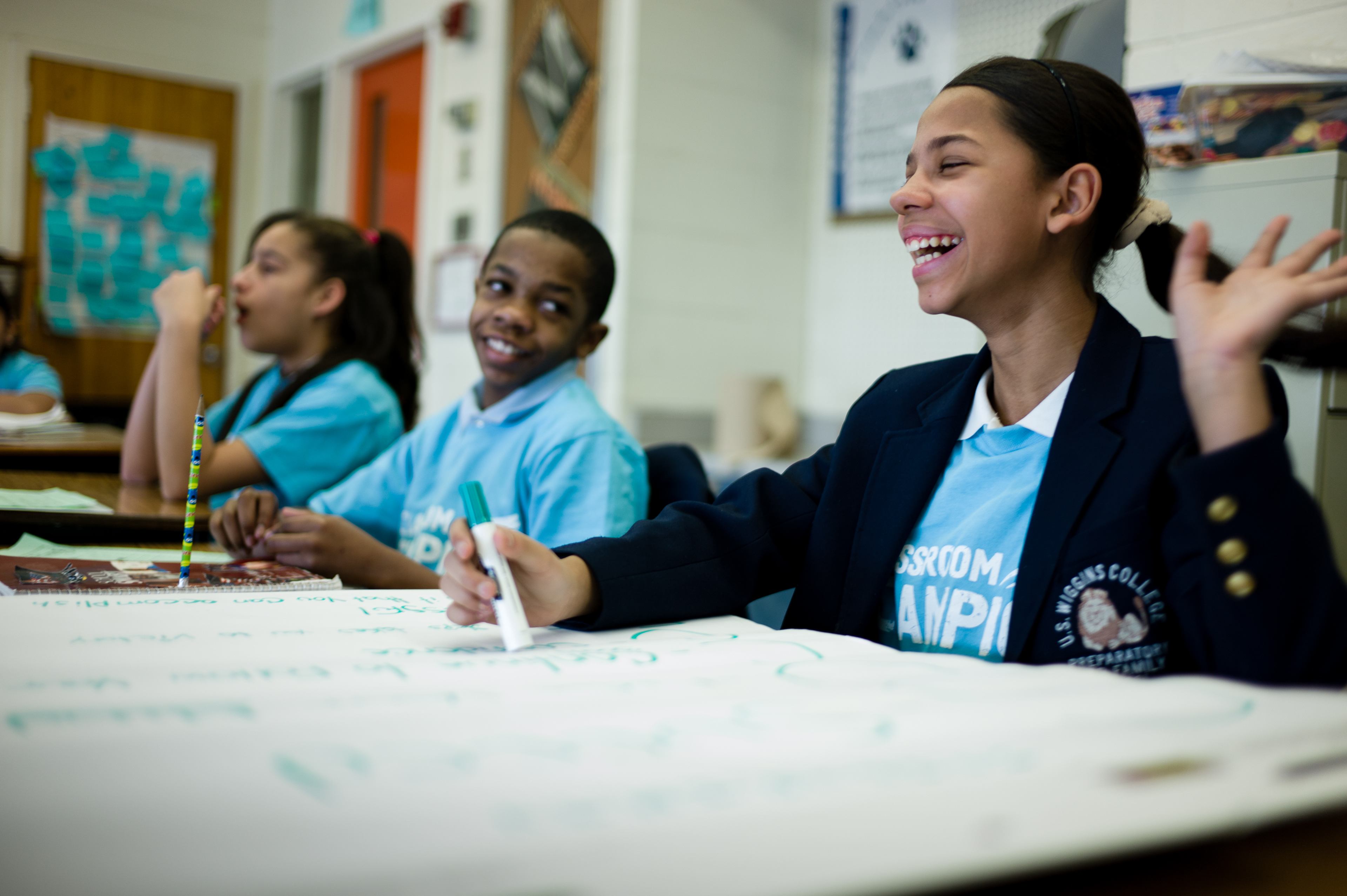 Students in Classroom Champions shirts write and laugh together during a classroom activity.