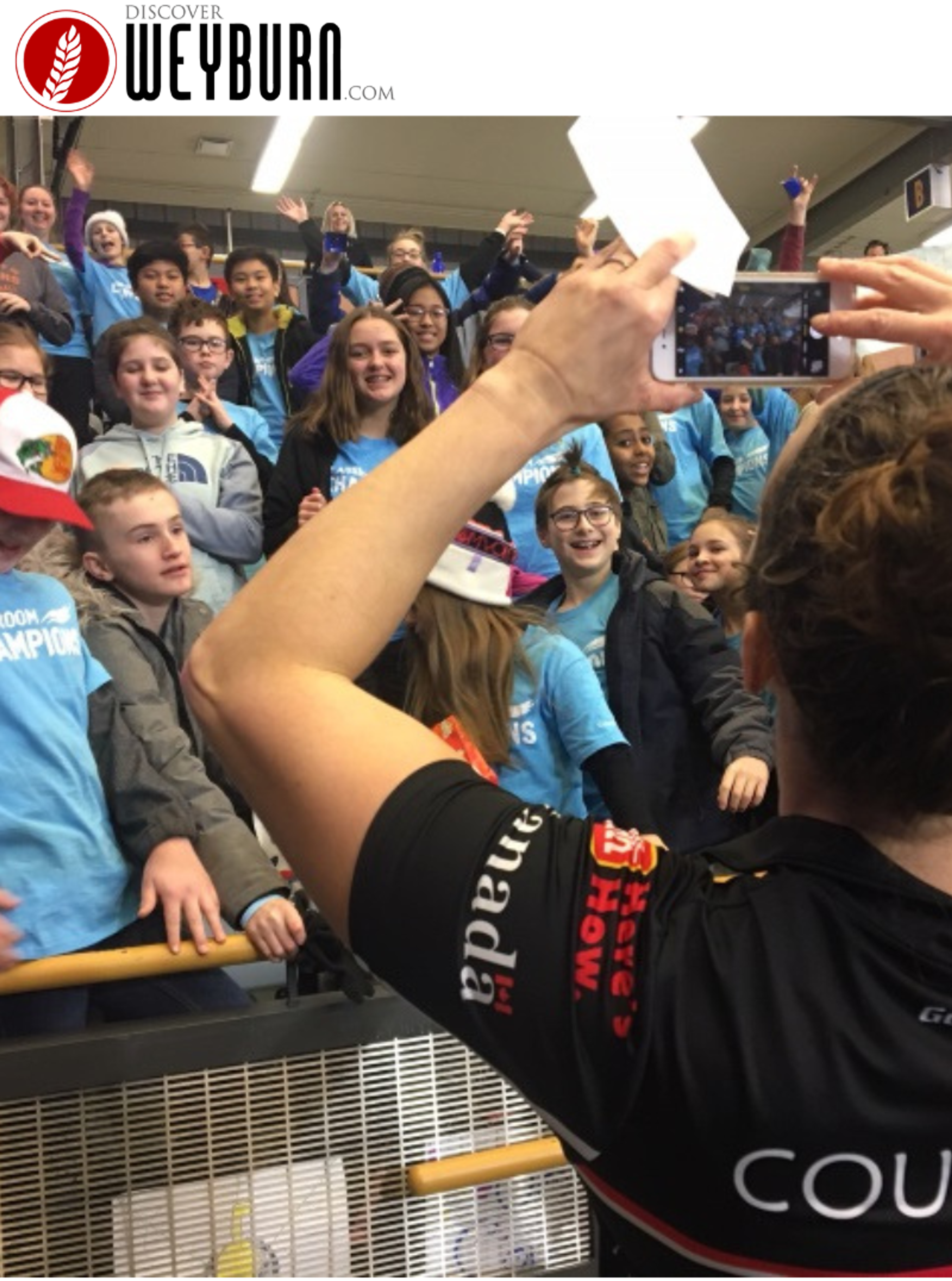 A Team Canada athlete takes a photo of cheering Classroom Champions students at an event.