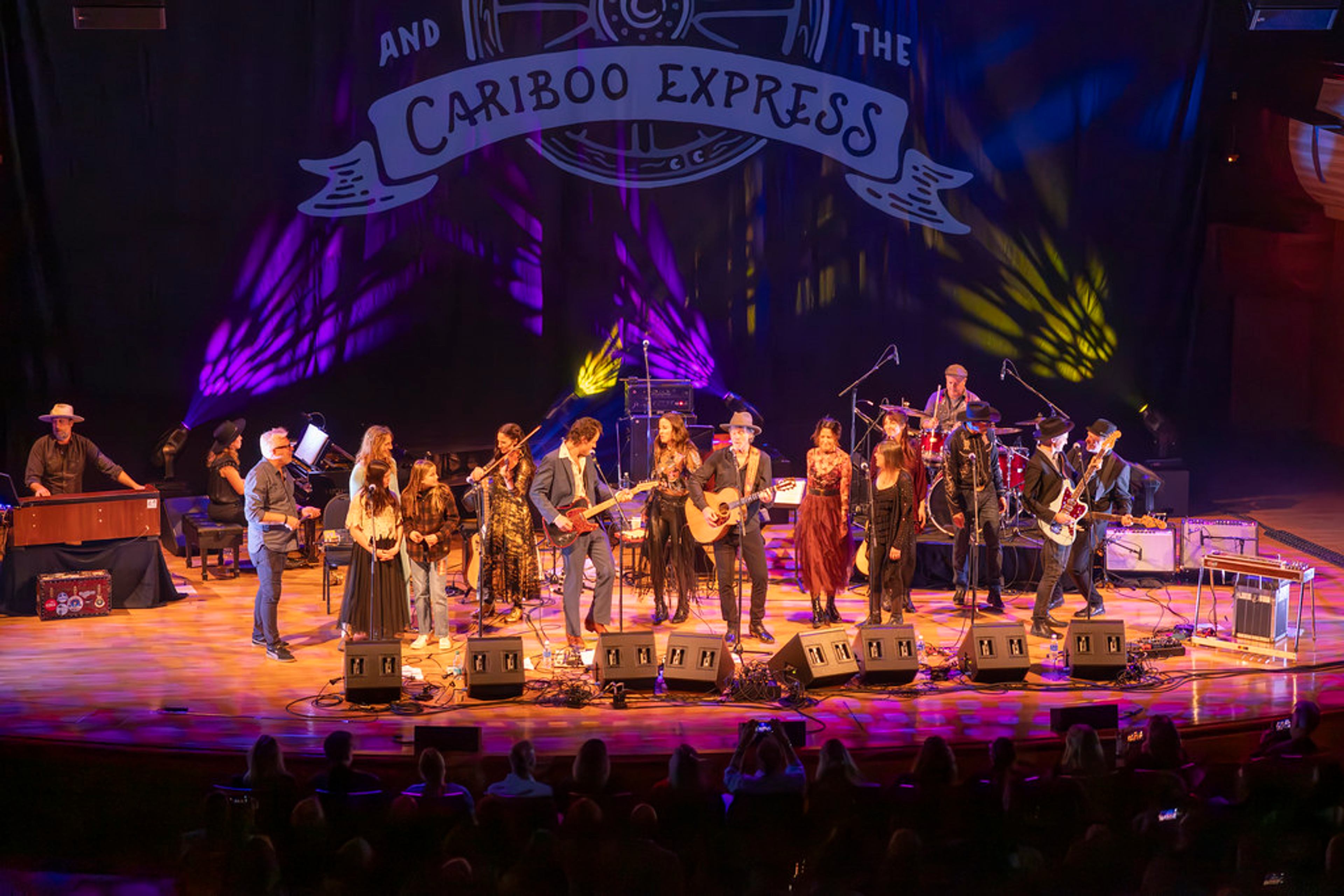 Musicians perform on stage at the Concert for Classrooms Calgary under a Cariboo Express banner.