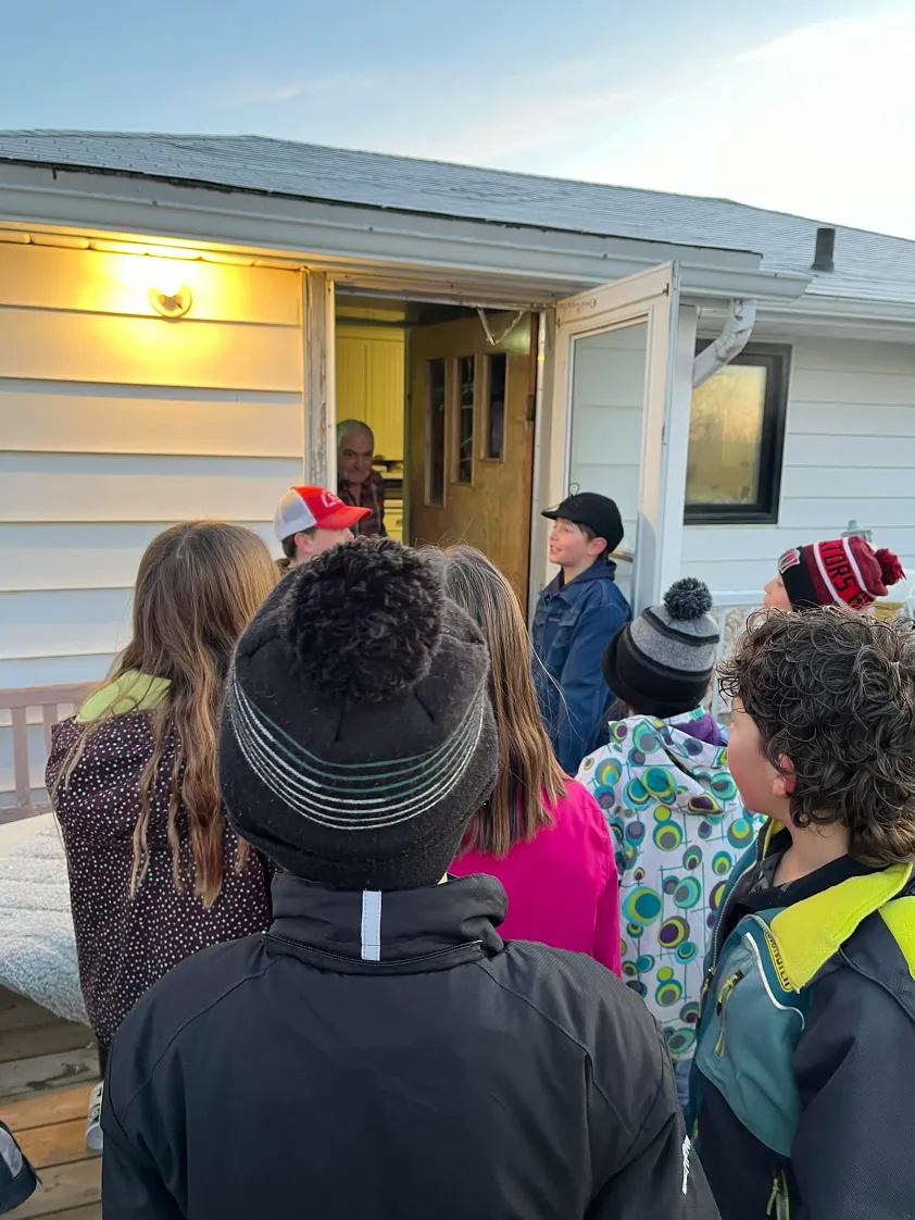 Students bundled in winter gear gather at a doorway to visit with a resident during a community service project.