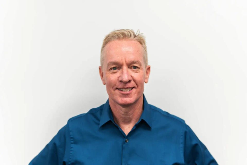 Headshot of a smiling man in a blue button-down shirt.