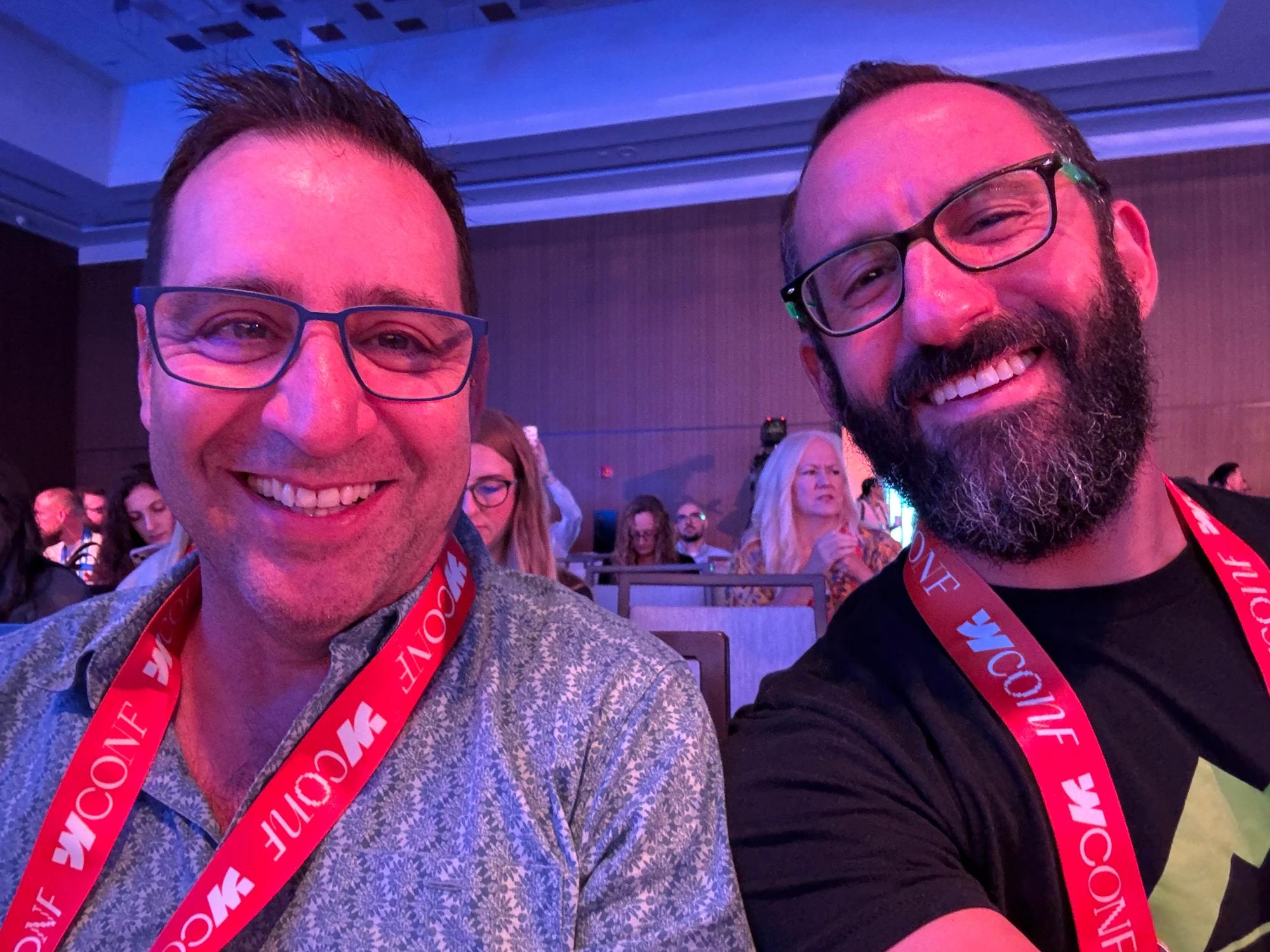 Jack (left) and David (right) smiling for a selfie at Webflow Conf 2026, wearing Scaler branded shirts and conference lanyards with attendees seated behind them.