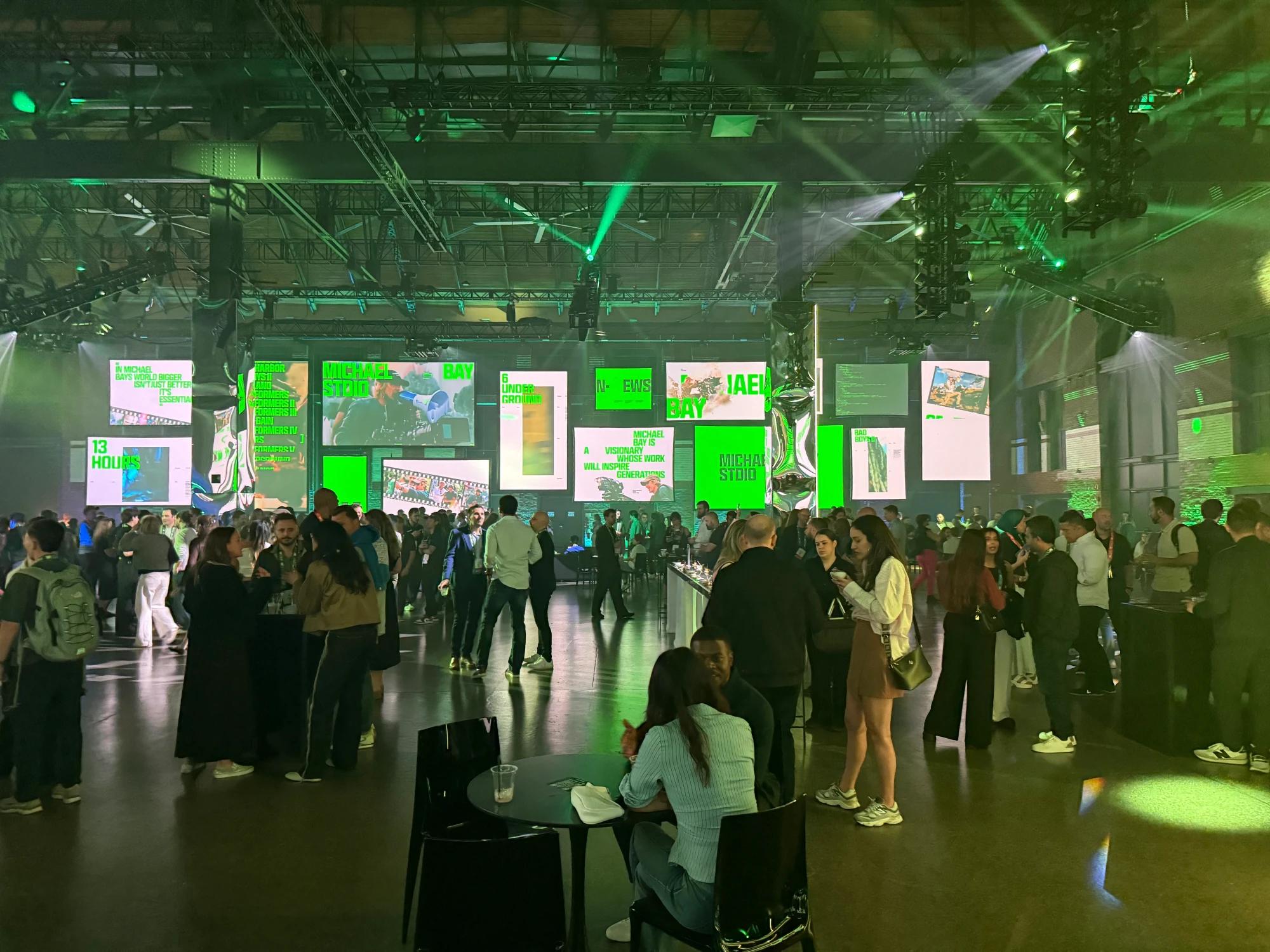 Attendees networking at Webflow Conf 2026 beneath green event lighting and large digital displays.