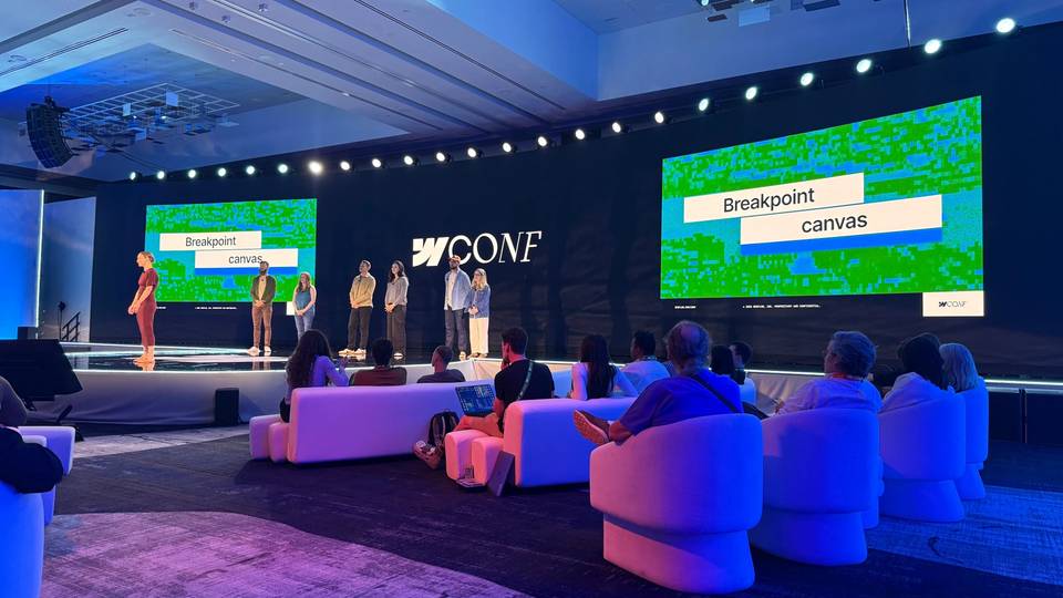 Presenters on stage at Webflow Conf, with screens displaying “Breakpoint canvas” and attendees seated in the foreground.