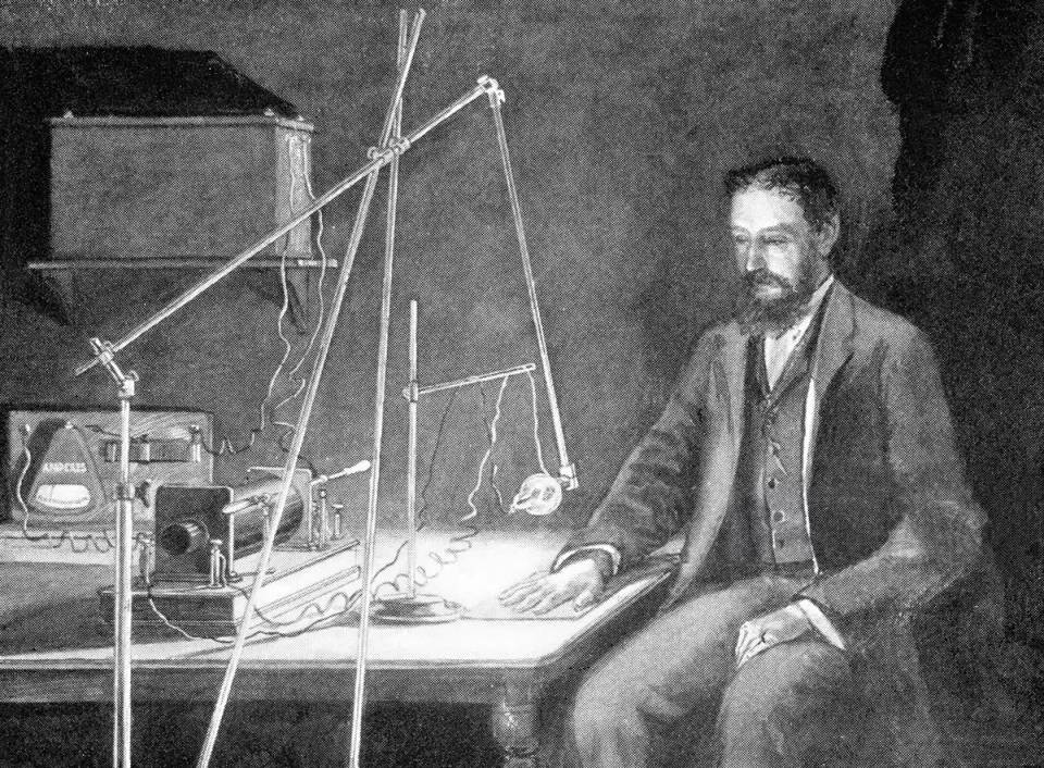 Black-and-white historical photo of Wilhelm Röntgen seated beside early X-ray laboratory equipment.
