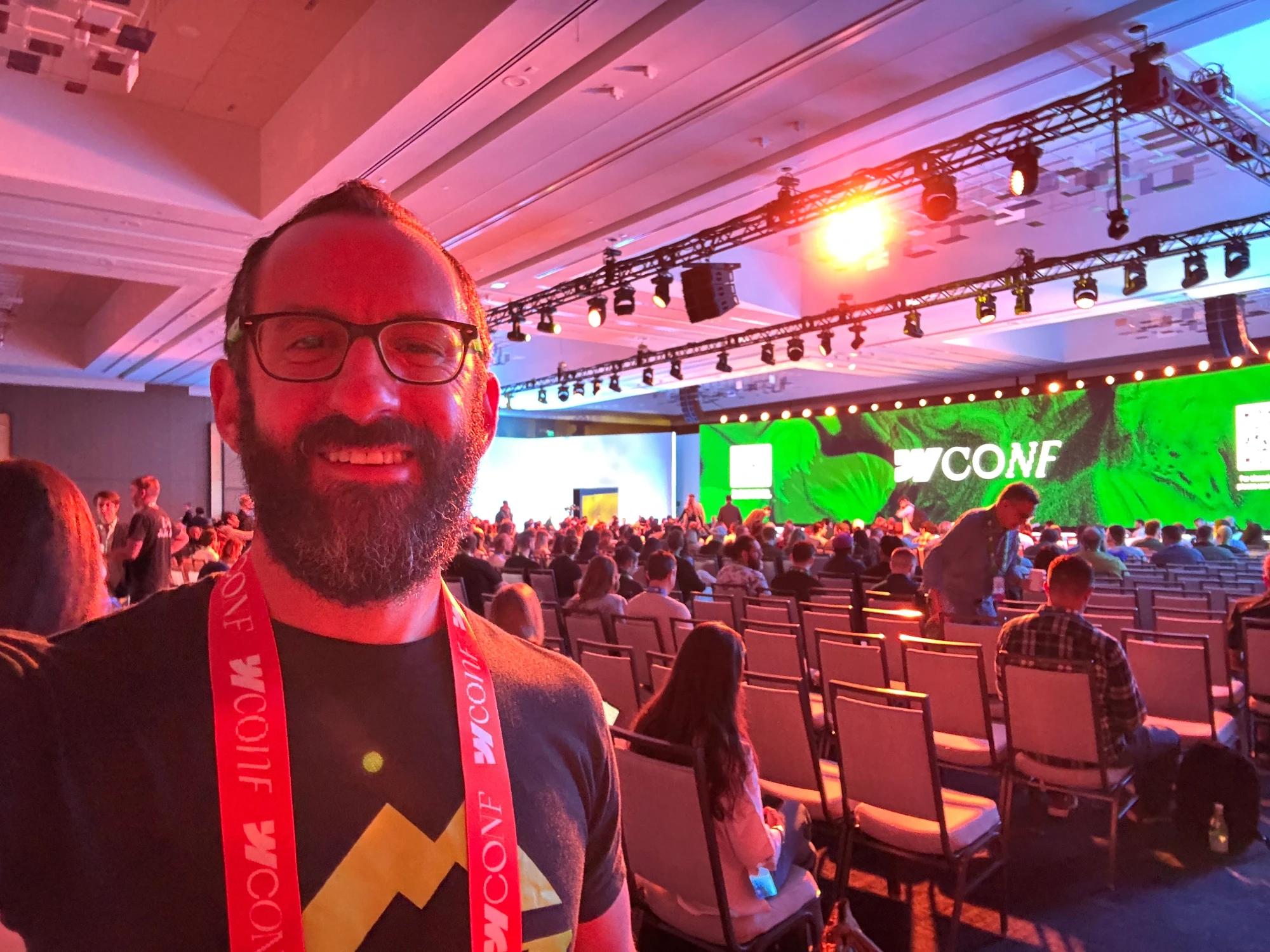 David smiling for a selfie at Webflow Conf 2026, wearing a Scaler branded shirt and conference lanyard with attendees seated behind him.