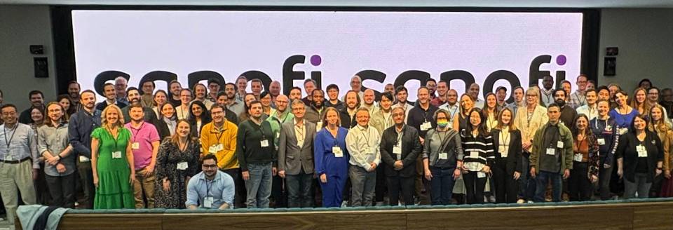 Group photo of NanoImaging Services symposium attendees standing in front of a large NIS logo screen.