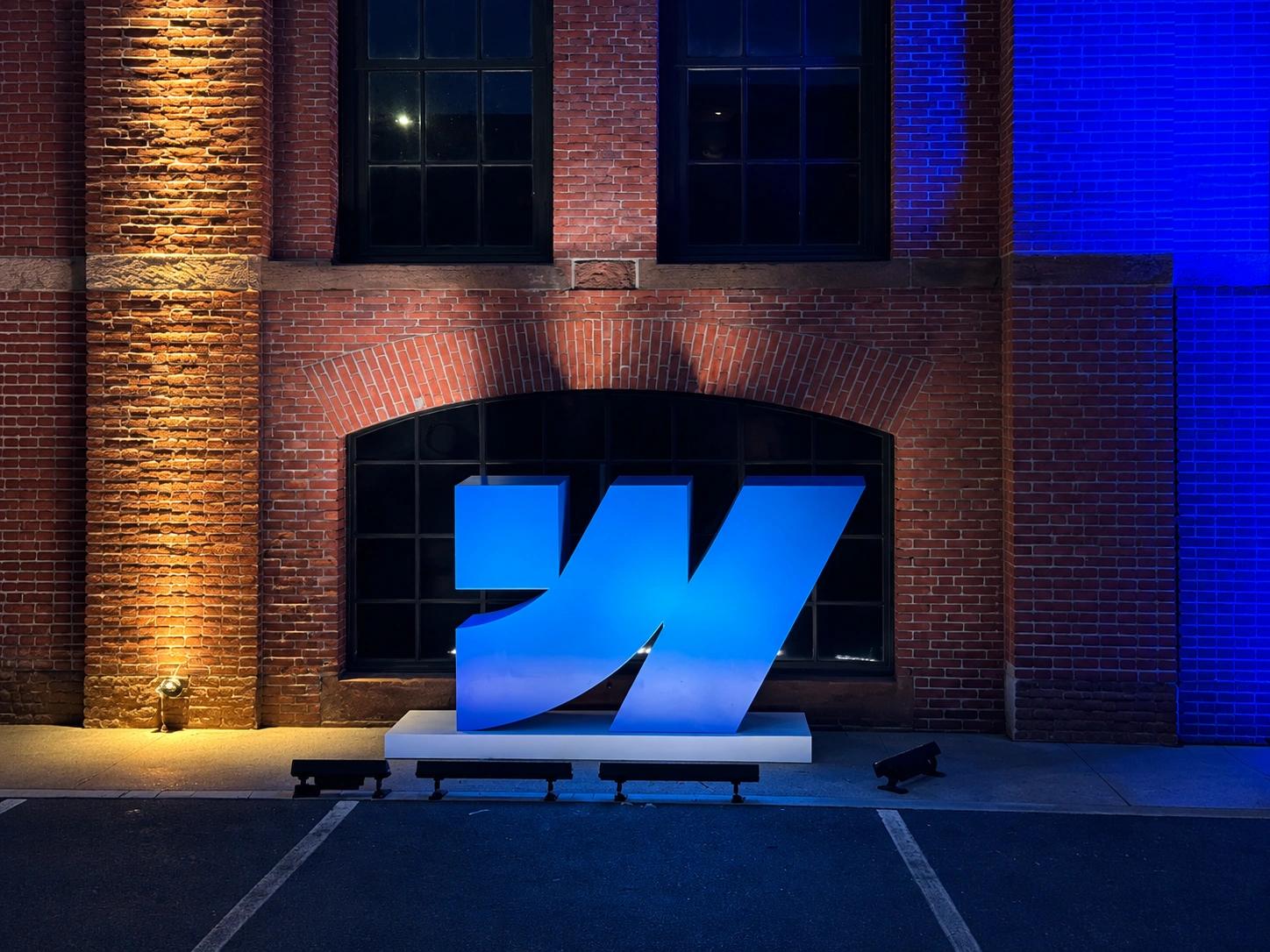 Large illuminated Webflow logo installation displayed against a brick wall at Webflow Conf 2026.
