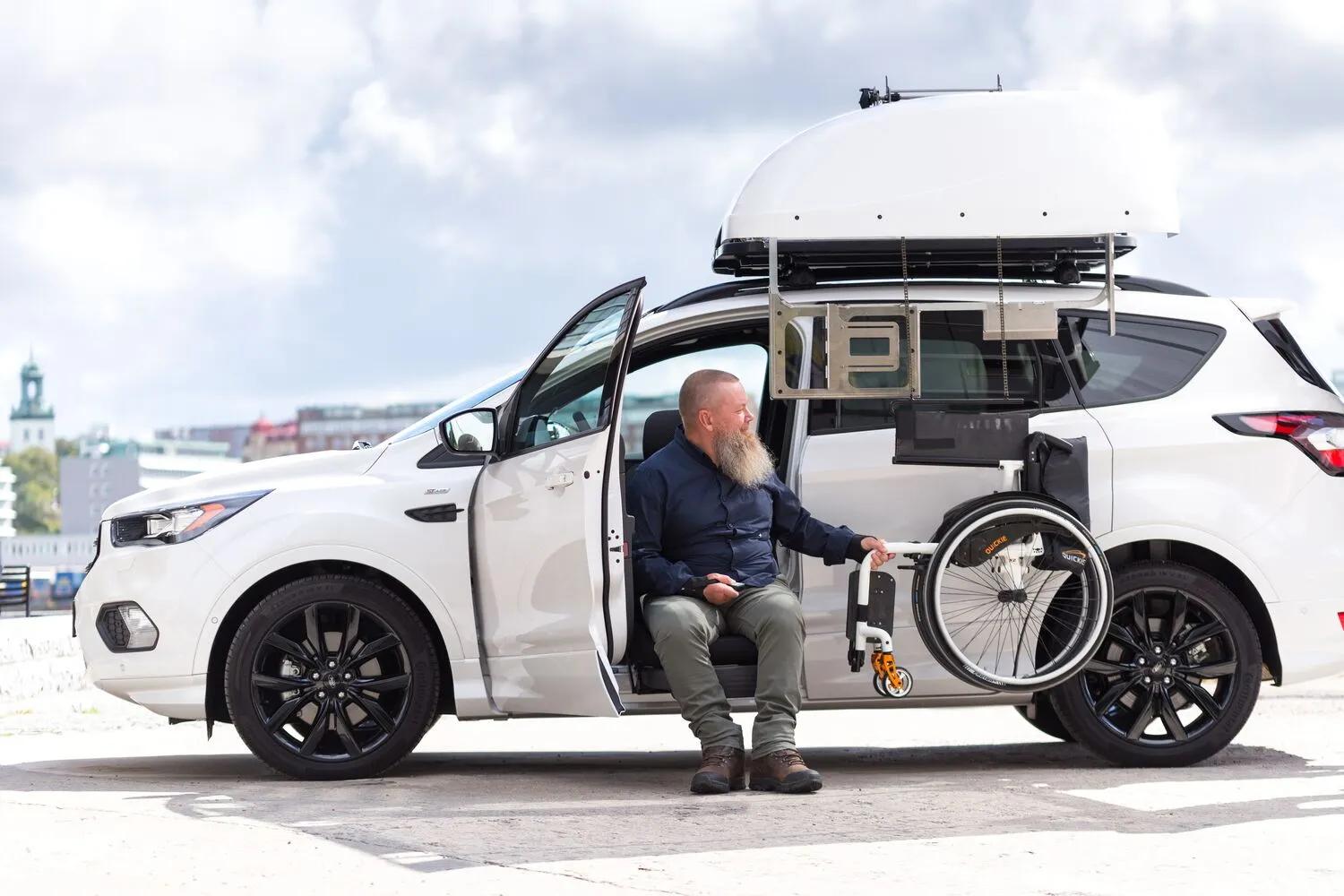 Gray car with Carony wheelchair transfer system, caregiver assisting user with footrest adjustment