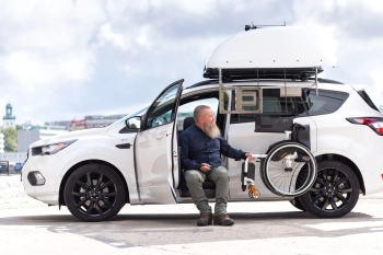 Gray car with Carony wheelchair transfer system, caregiver assisting user with footrest adjustment