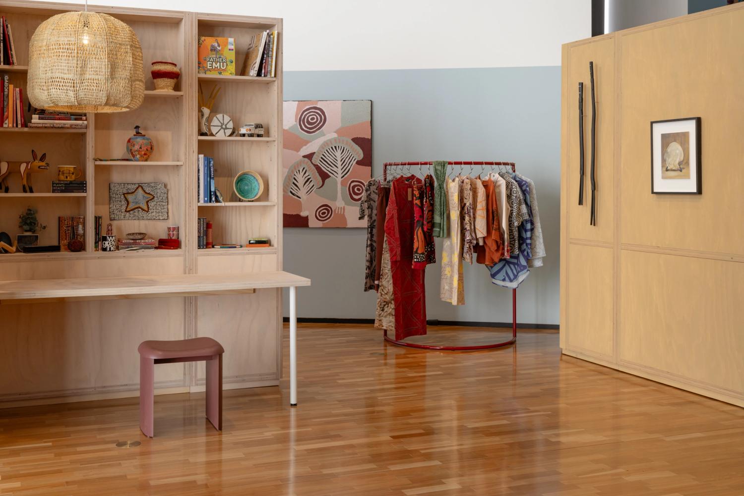 Bedroom with study nook including filled shelves, hanging clothing a woven pendant light and artwork.