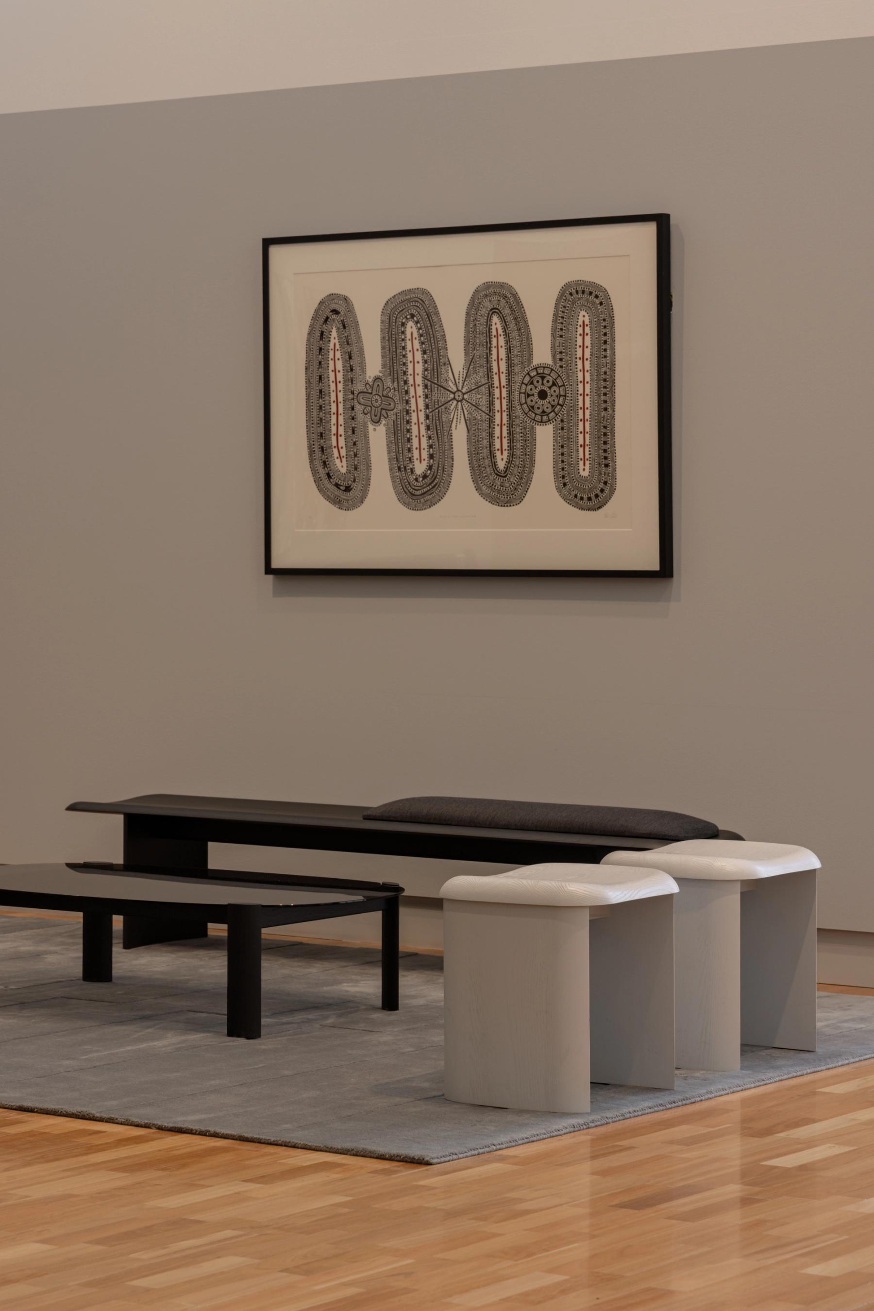Living space with wall art, bench, low stools, coffee table and rug on a wooden floor. 