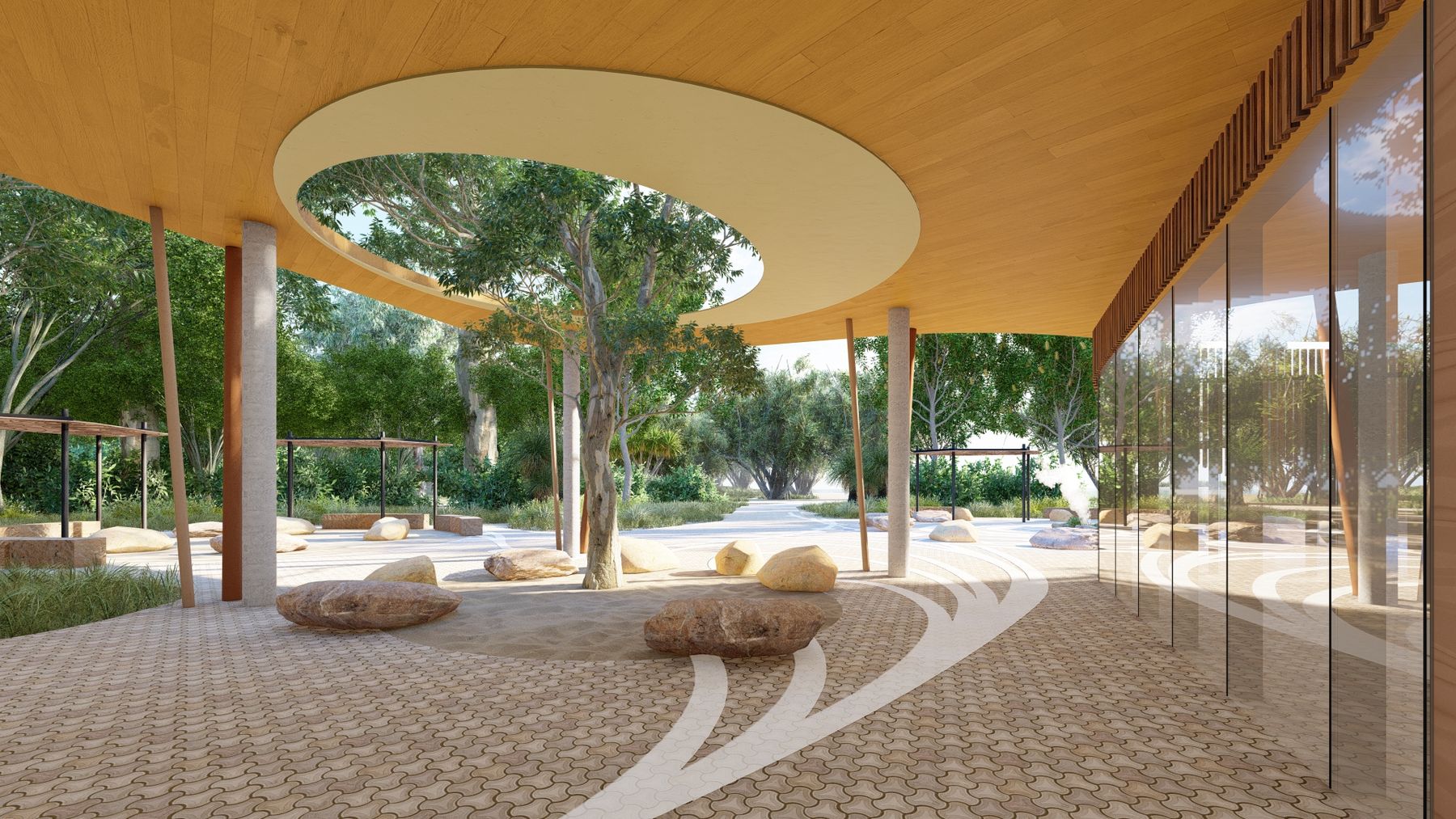 Open courtyard with patterned stone paving and scattered sandstone rocks, featuring a tree growing through a circular cut-out in a timber ceiling, surrounded by glass walls and greenery.